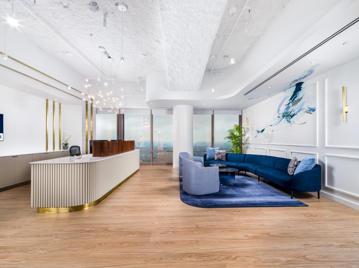 JAMS Atlanta reception — curved fluted cream desk with brass base, galaxy-cluster chandelier, blue abstract painting, and a navy sectional lounge on a deep blue rug.