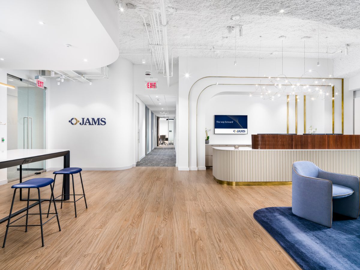 JAMS Atlanta lobby wide-angle — JAMS wordmark on white wall, curved fluted reception desk on right, navy stools at left counter, and a hallway between.