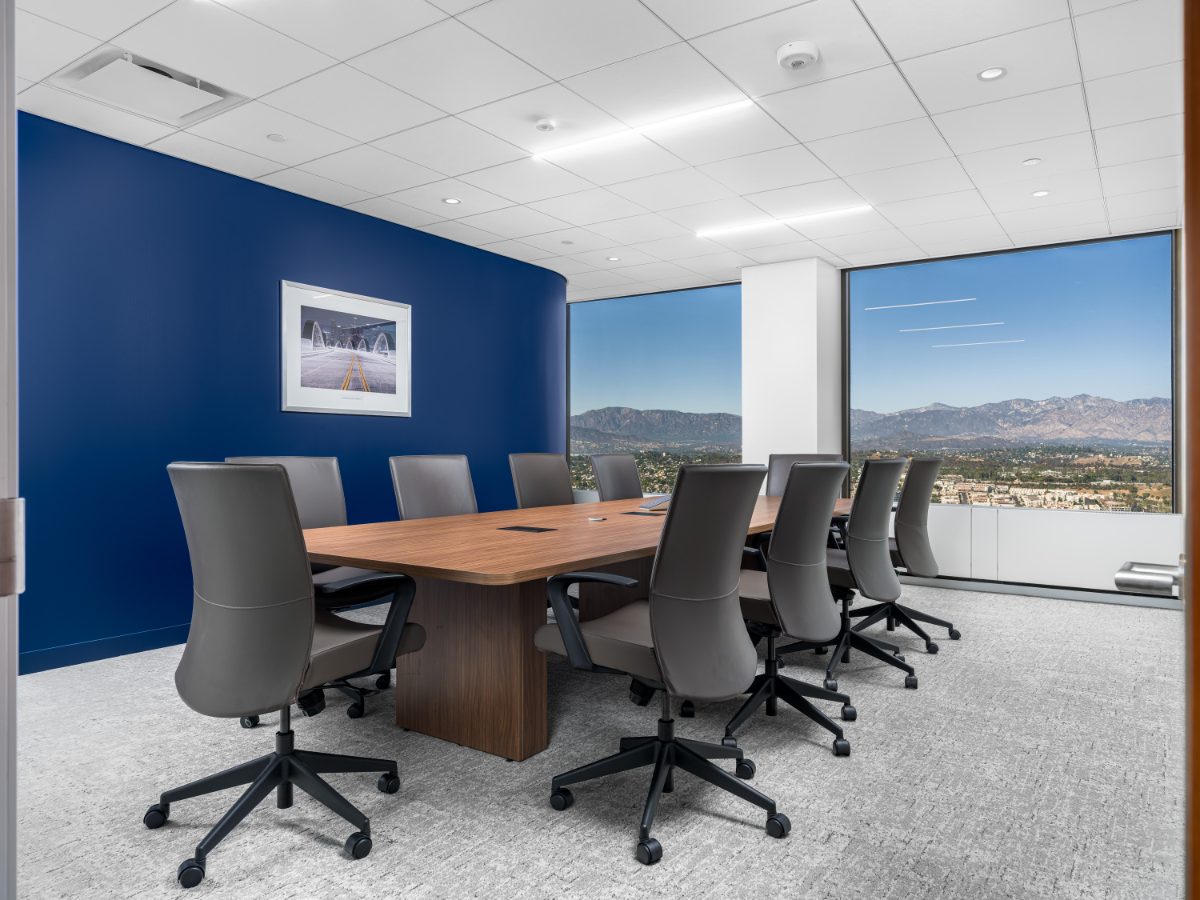 Conference Room 01 at JAMS Los Angeles — walnut table, grey leather chairs, cobalt curved wall with 6th Street Viaduct print, and San Gabriel Mountain windows.