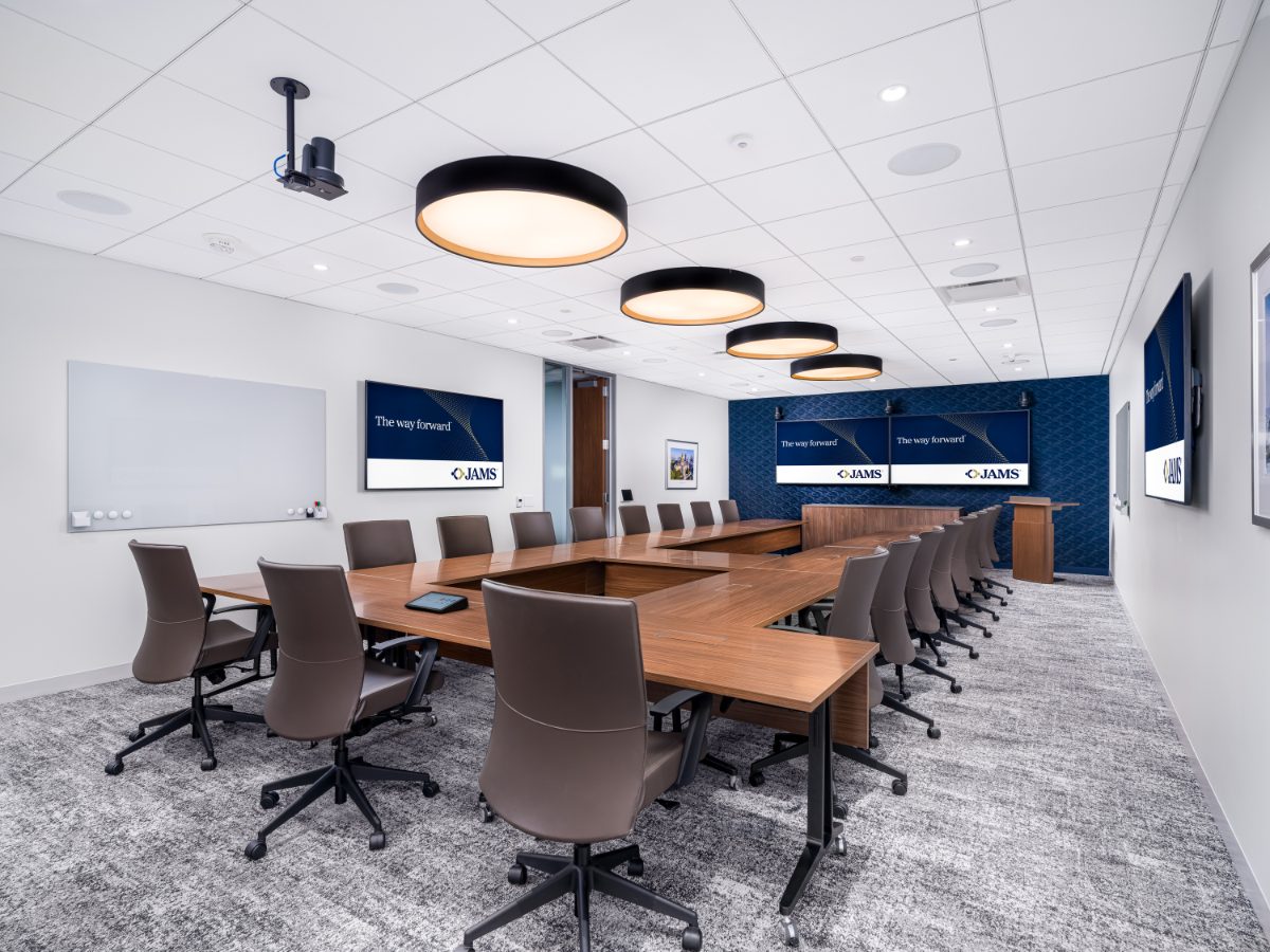 JAMS Atlanta Board Room 01 at Promenade Tower — U-shaped walnut conference table, brown leather chairs, four drum pendants, navy patterned wall with displays.