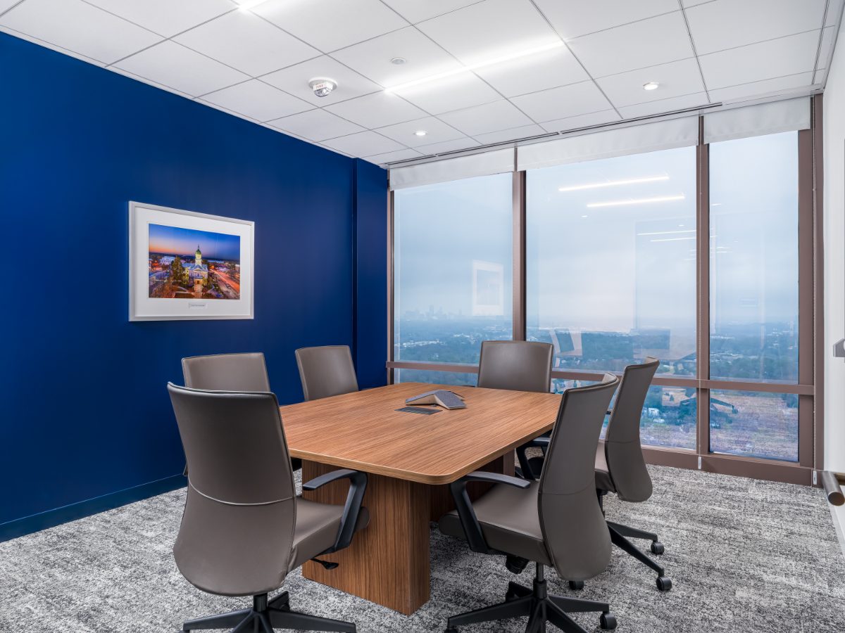 JAMS Atlanta small conference room at Promenade Tower — walnut table, grey leather chairs, cobalt wall with framed Atlanta photo, hazy Atlanta skyline window.
