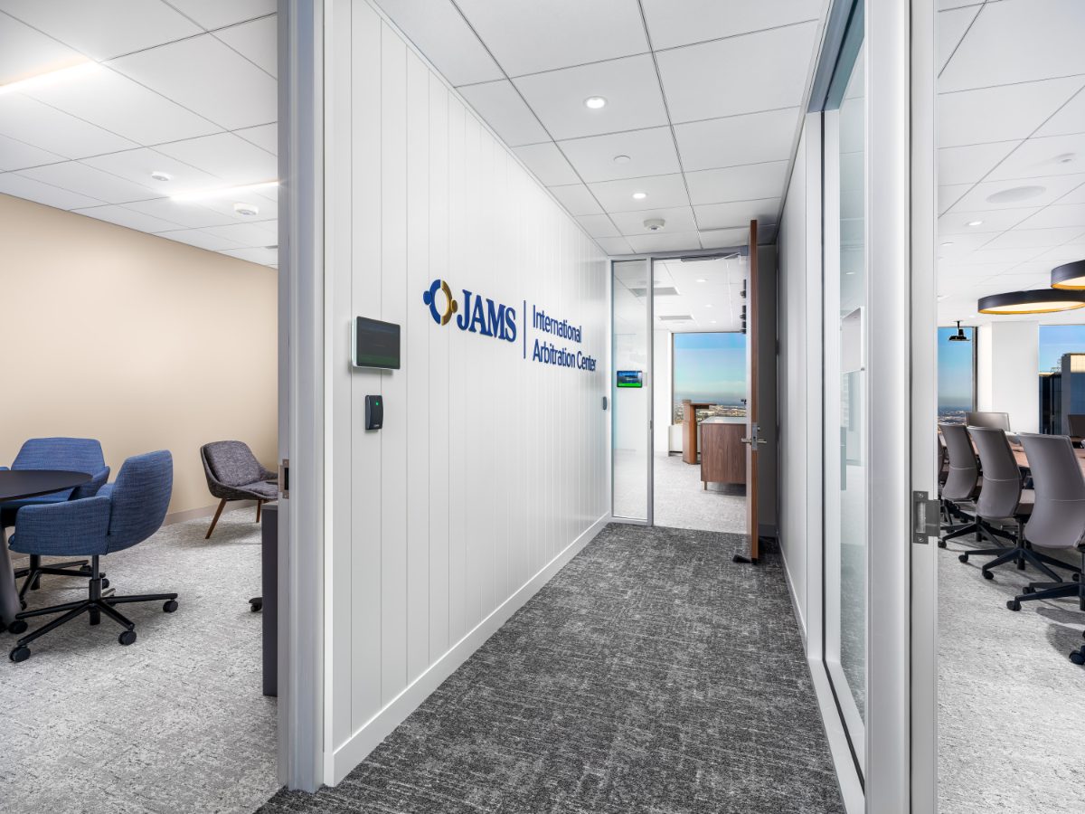 Corridor to JAMS International Arbitration Center, Los Angeles — white slatted wall with blue JAMS sign, glassed conference room on right, blue lounge on left.