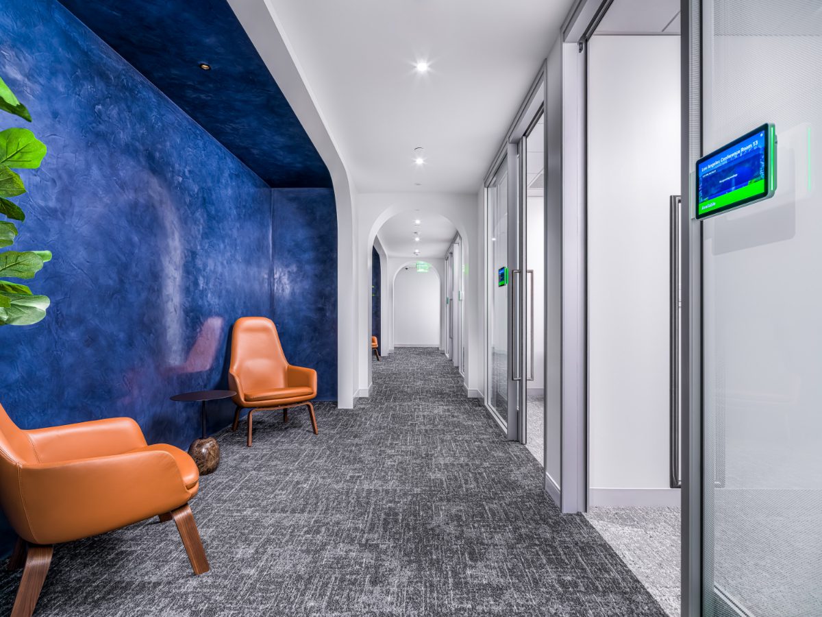 JAMS LA hallway lounge — two cognac leather chairs against a cobalt Venetian-plaster wall with a curved reveal, opening onto an arched white corridor.