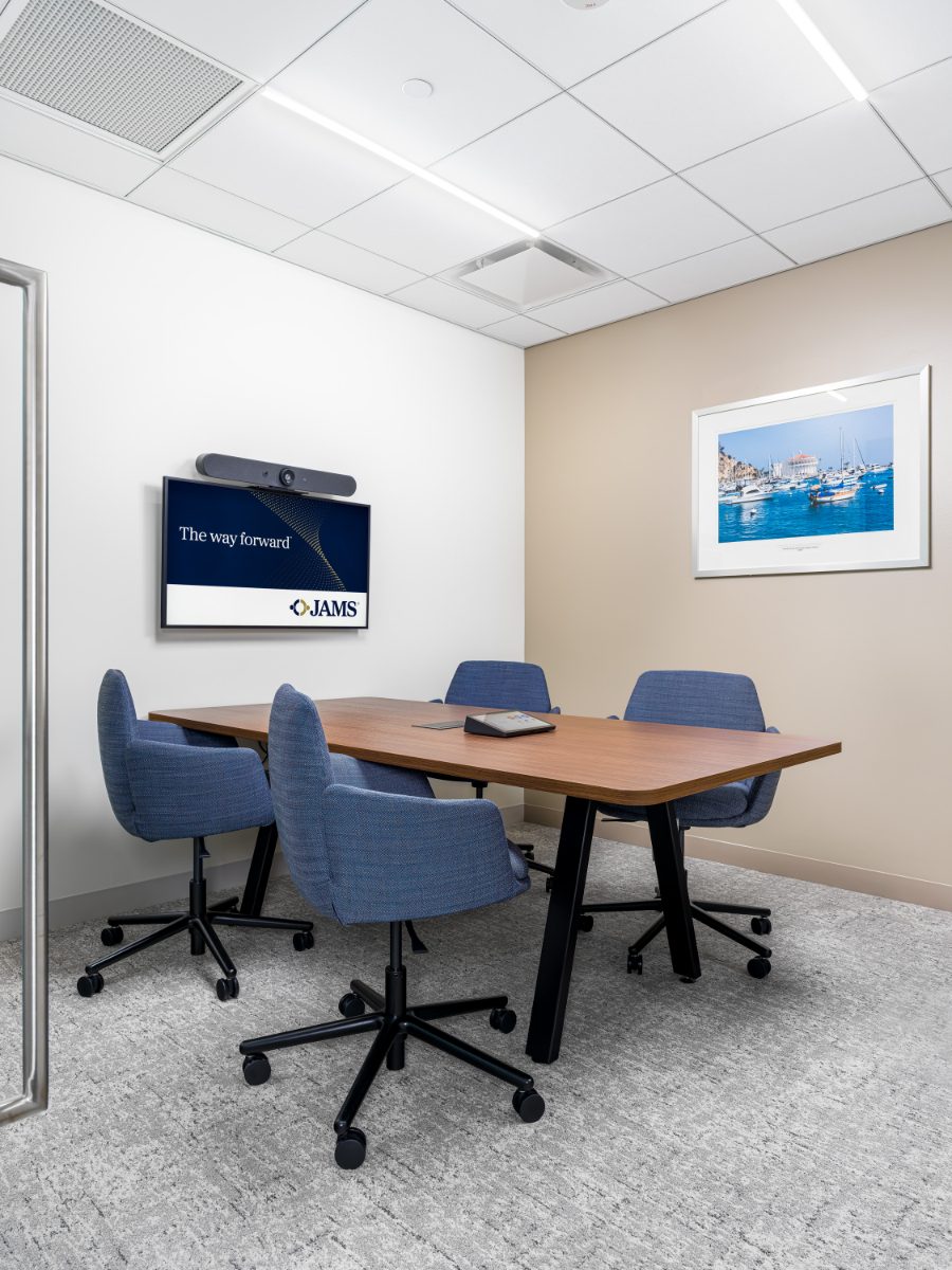 Small caucus room at JAMS Los Angeles — four periwinkle tweed swivel chairs around a walnut table, JAMS-branded display, framed Avalon Harbor print on a warm beige wall.