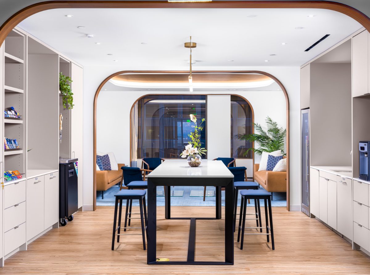JAMS LA cafe and lounge — black-and-quartz high-top with blue stools and brass pendant in front, cognac sofas and blue chairs in the lounge through a walnut arch.