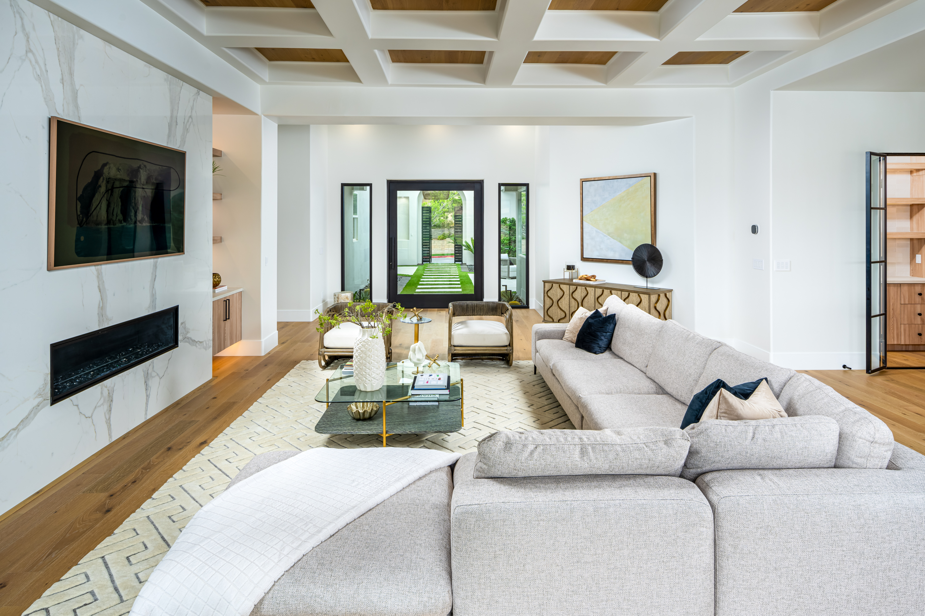 Living Room at a Stately modern transitional luxury home in Las Vegas (1533 TS) — white-and-wood coffered ceiling, marble fireplace, grey sectional, corduroy stools.