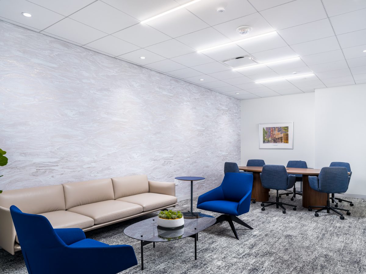 JAMS Atlanta relaxed meeting room at Promenade Tower — cream sofa, blue tub chairs, glass coffee table, conference table with blue chairs, marble-veined feature wall.