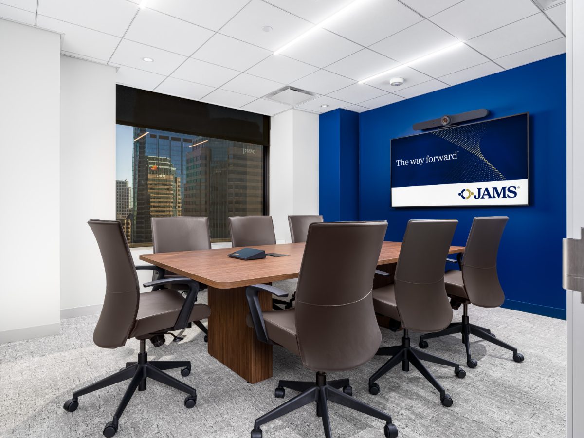 JAMS LA Conference Room 24 — walnut table, charcoal leather chairs, cobalt feature wall behind a JAMS-branded display, downtown LA tower through the window.