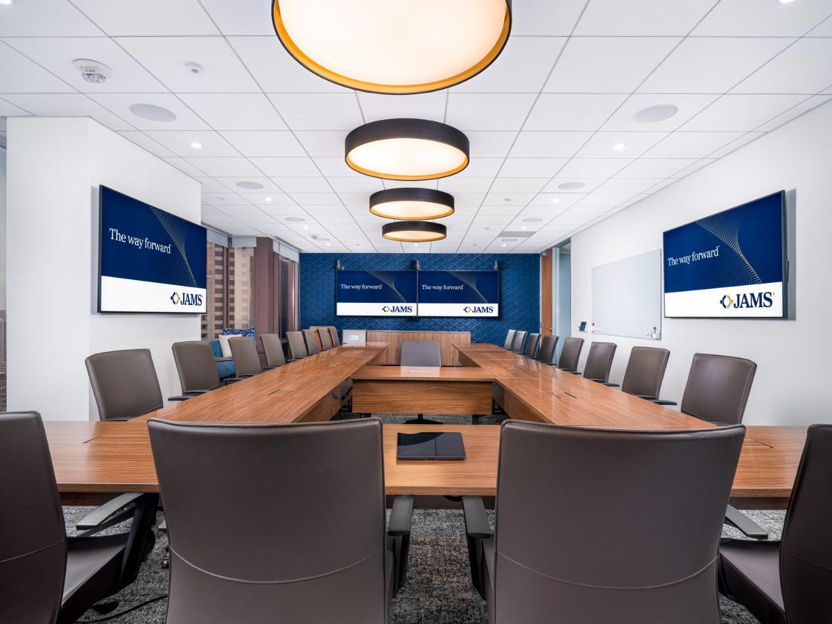 JAMS Atlanta large board room at Promenade Tower — U-shaped walnut table, brown leather chairs, three drum pendants, navy patterned wall with dual displays.