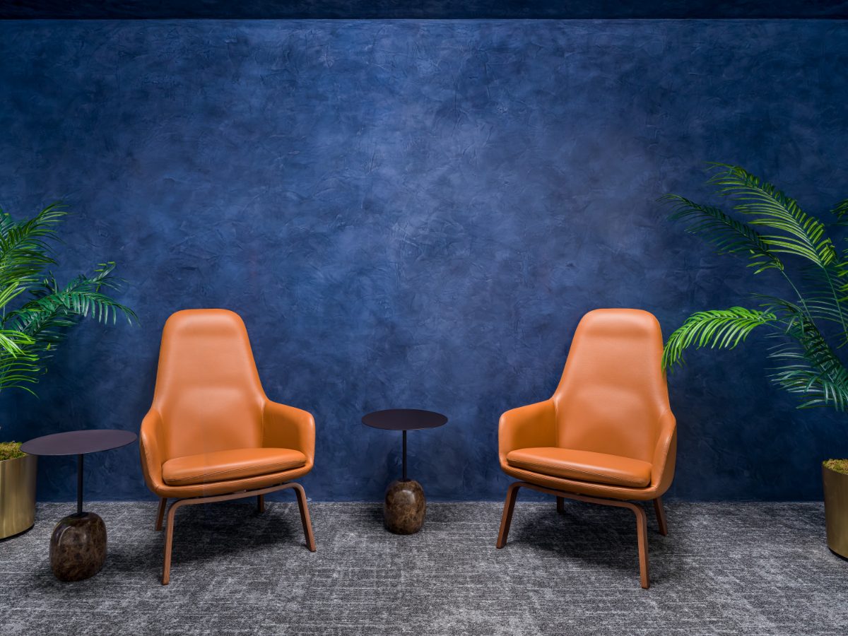JAMS LA hallway nook — two cognac leather lounge chairs flank black-and-marble side tables against a cobalt Venetian-plaster wall framed by palm fronds.