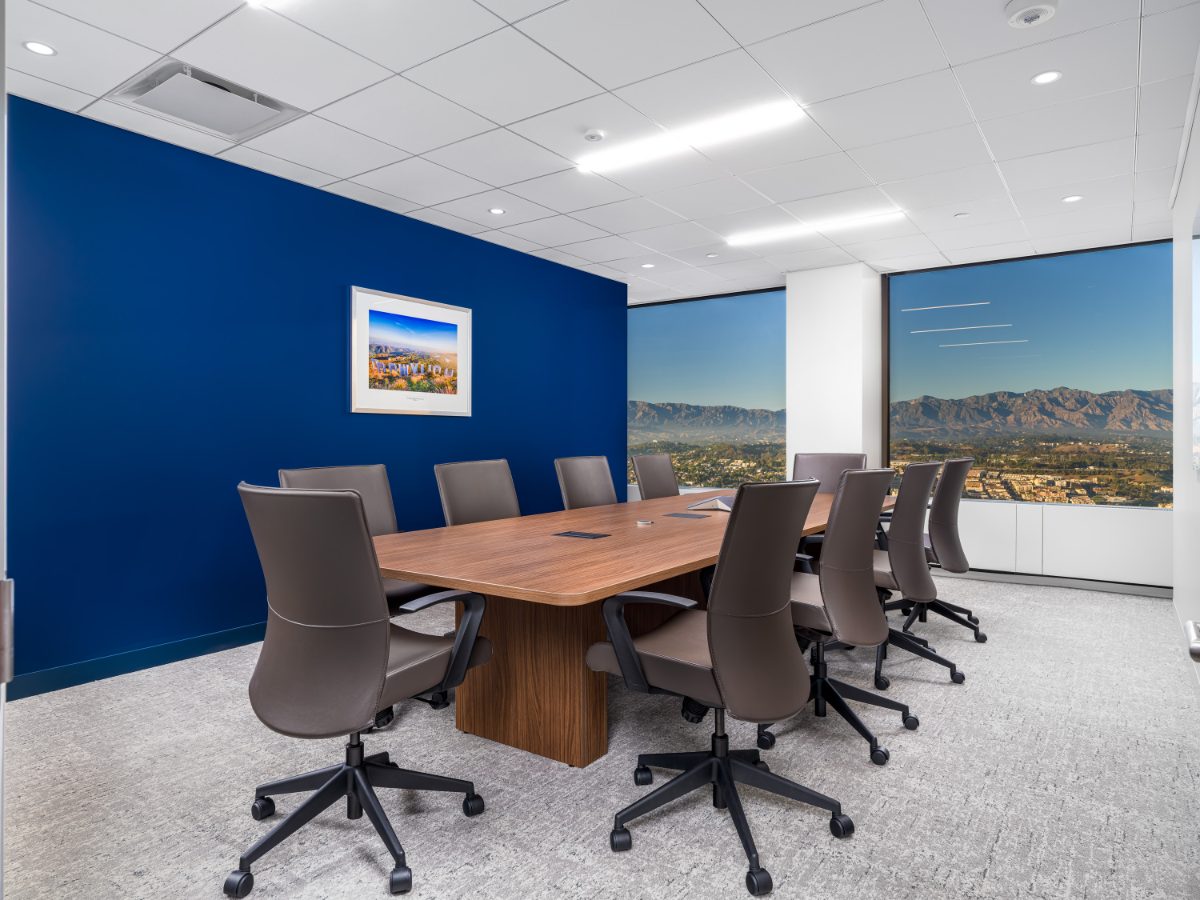 JAMS LA Conference Room 37 at golden hour — walnut table, charcoal leather chairs, cobalt wall with Hollywood sign print, San Gabriels glowing through the window.