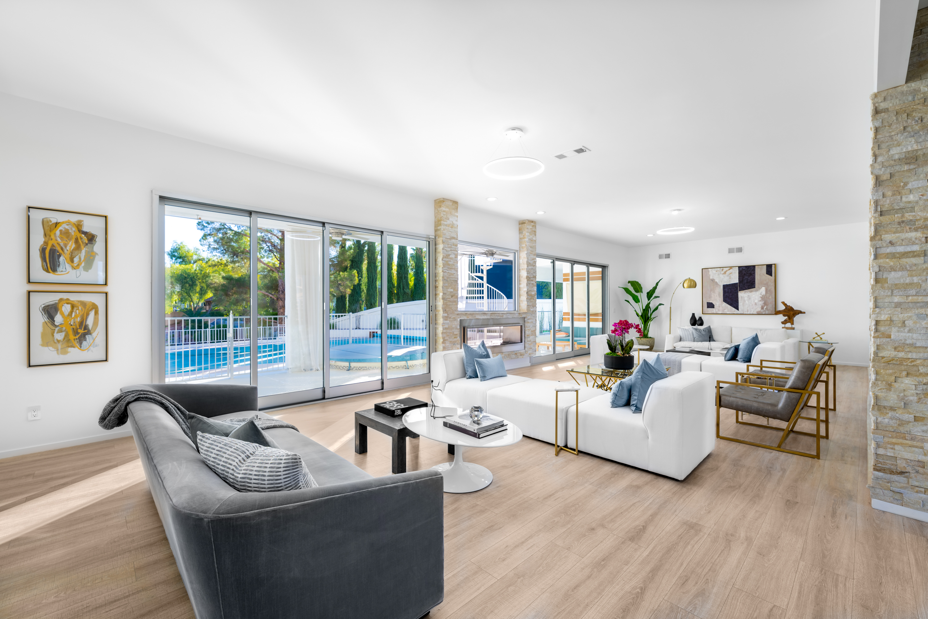 Living Room at a Stately modern poolside home in Las Vegas (2824 HSC) — sliding pool glass, mustard yellow art, brass-and-stone tables, grey velvet sofa.