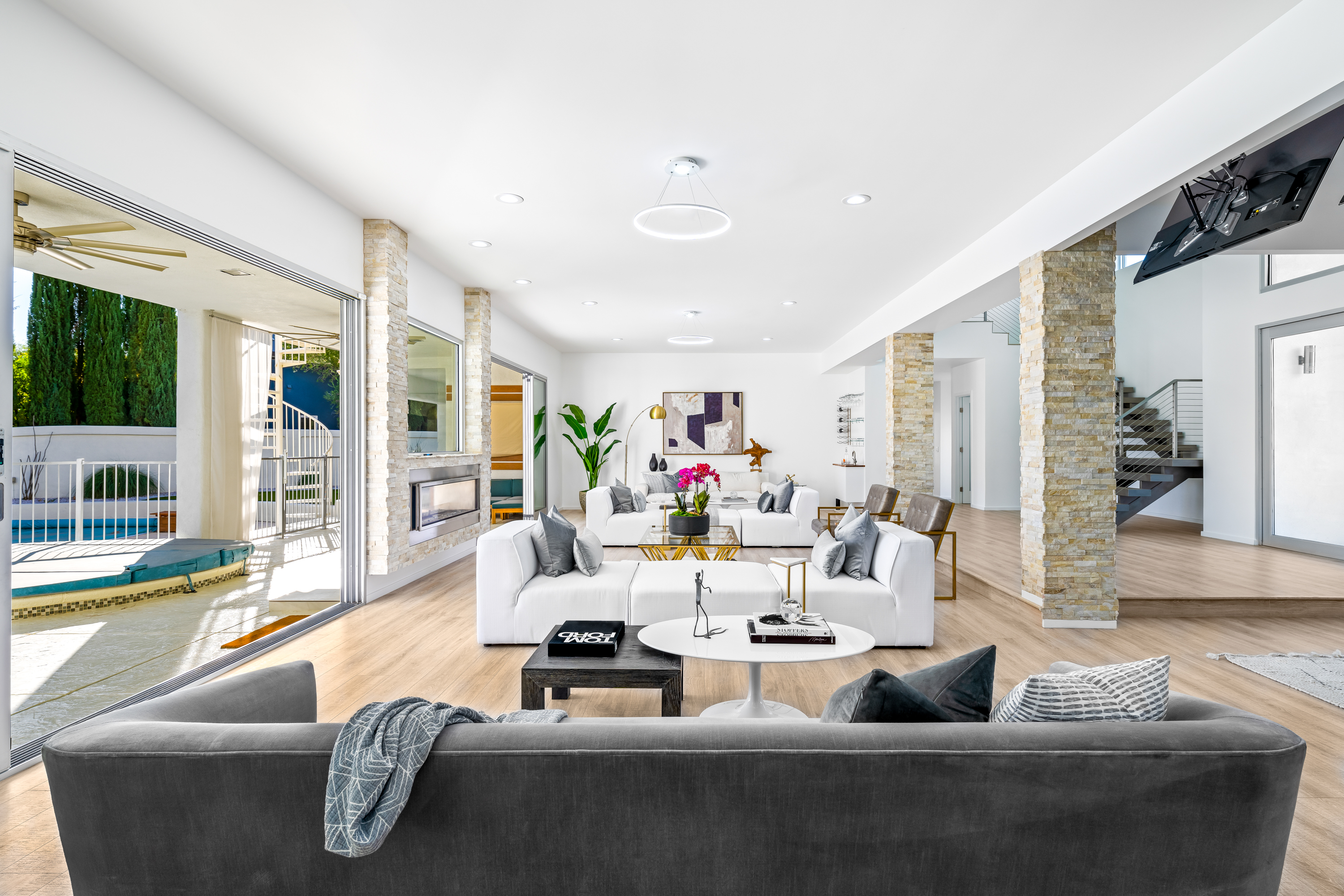 Living Room at a Stately modern poolside home in Las Vegas (2824 HSC) — sliding pool glass, mustard yellow art, brass-and-stone tables, grey velvet sofa.