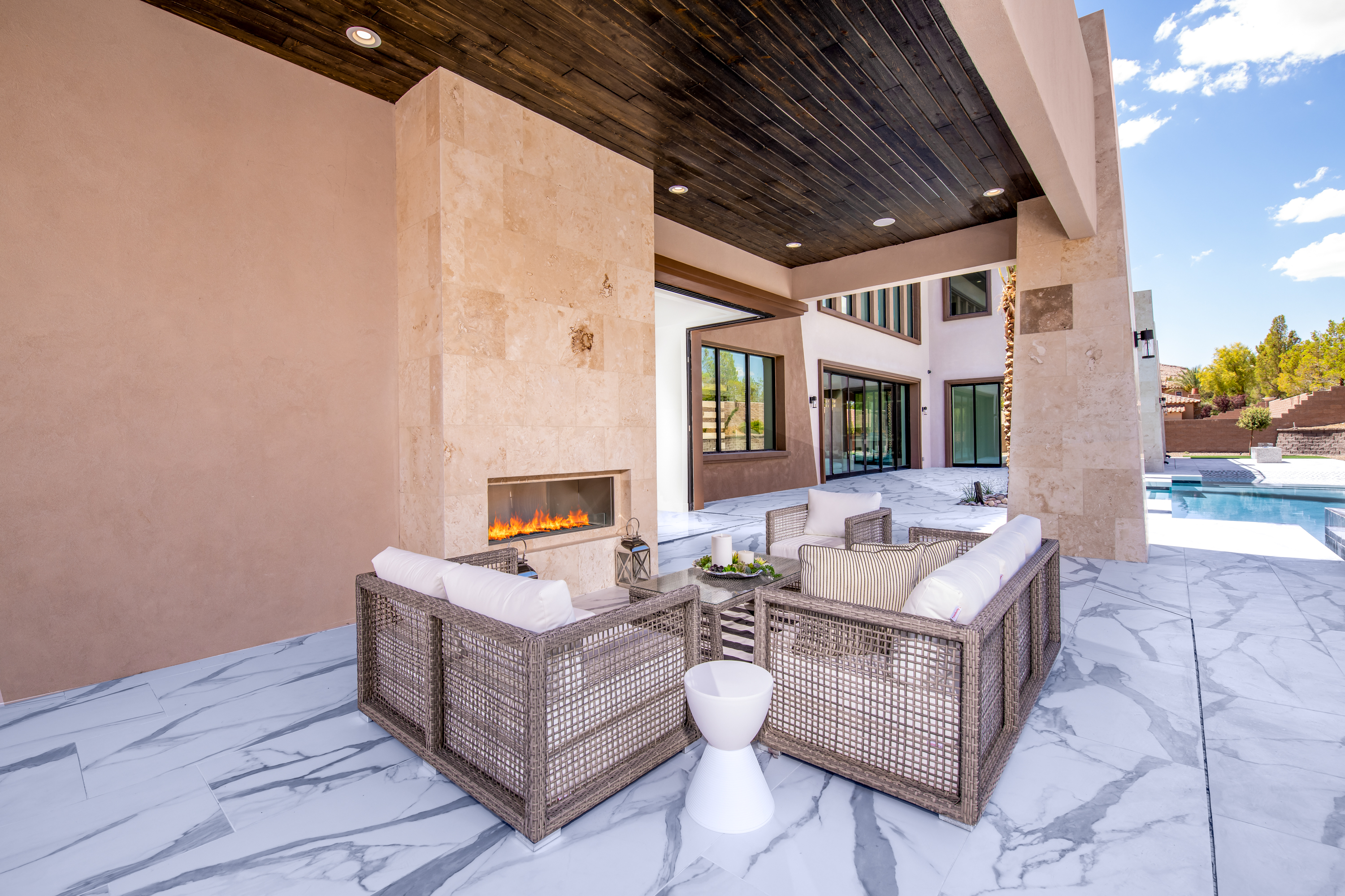 Outdoor Living Area at a Stately modern desert resort home in Las Vegas (38 RA) — marble fireplace surround, walnut accent stool, abstract art, palm view.