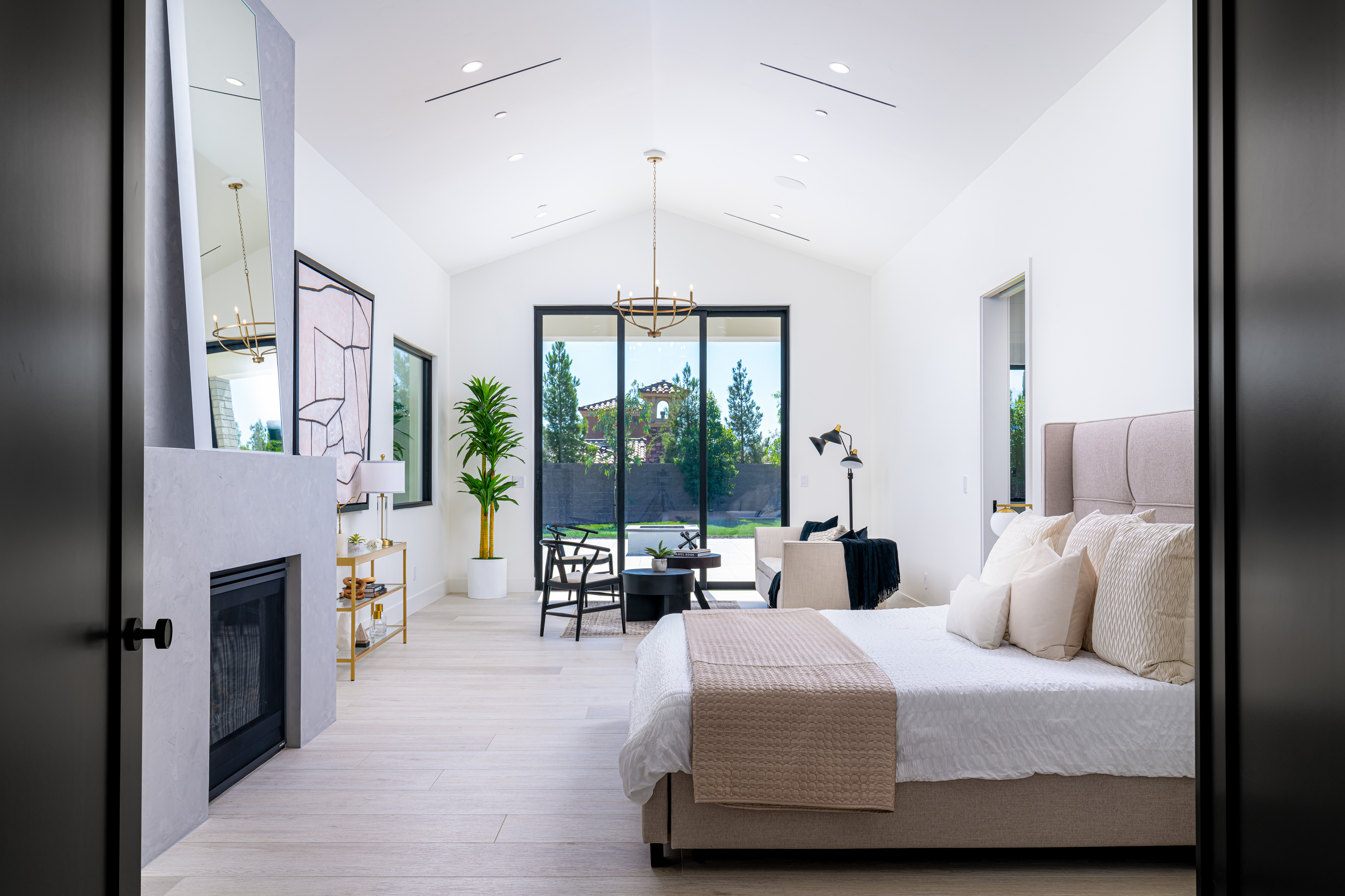 Master Bedroom at a Stately Vegas-luxury indoor-outdoor home in Las Vegas (16 CHC) — wagon-wheel chandelier, tufted ottoman, pleated barrel chairs, pool view.