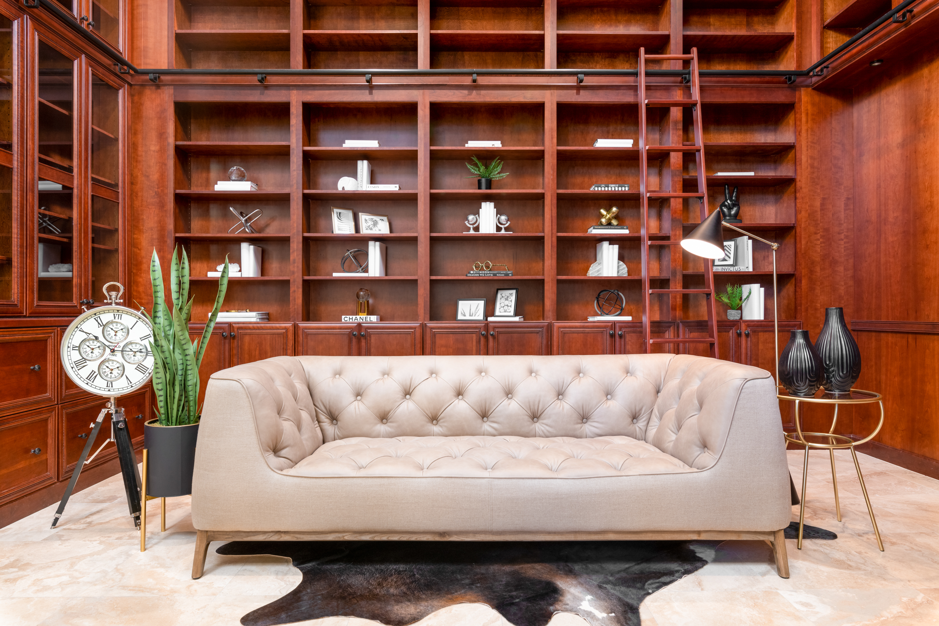 Library at a Stately traditional gentleman's library home in Las Vegas (2297 FA) — cherry bookcases, rolling library ladder, tufted cream sofa, antique tripod clock.
