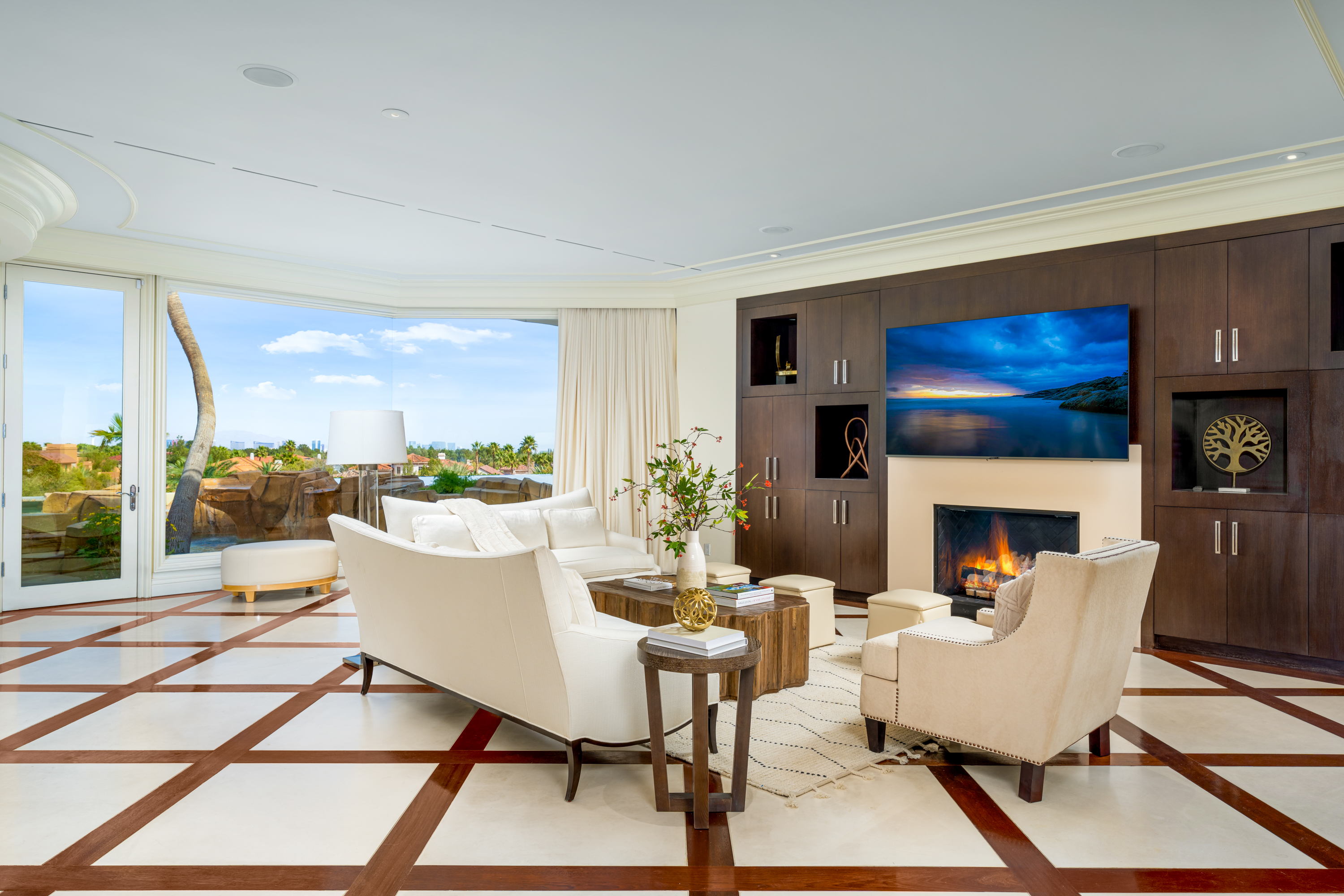 Living Room at a Stately glam estate home in Las Vegas (5114 SHD) — two-story curtains, paired gold-base ottomans, marble fireplace, panoramic view.