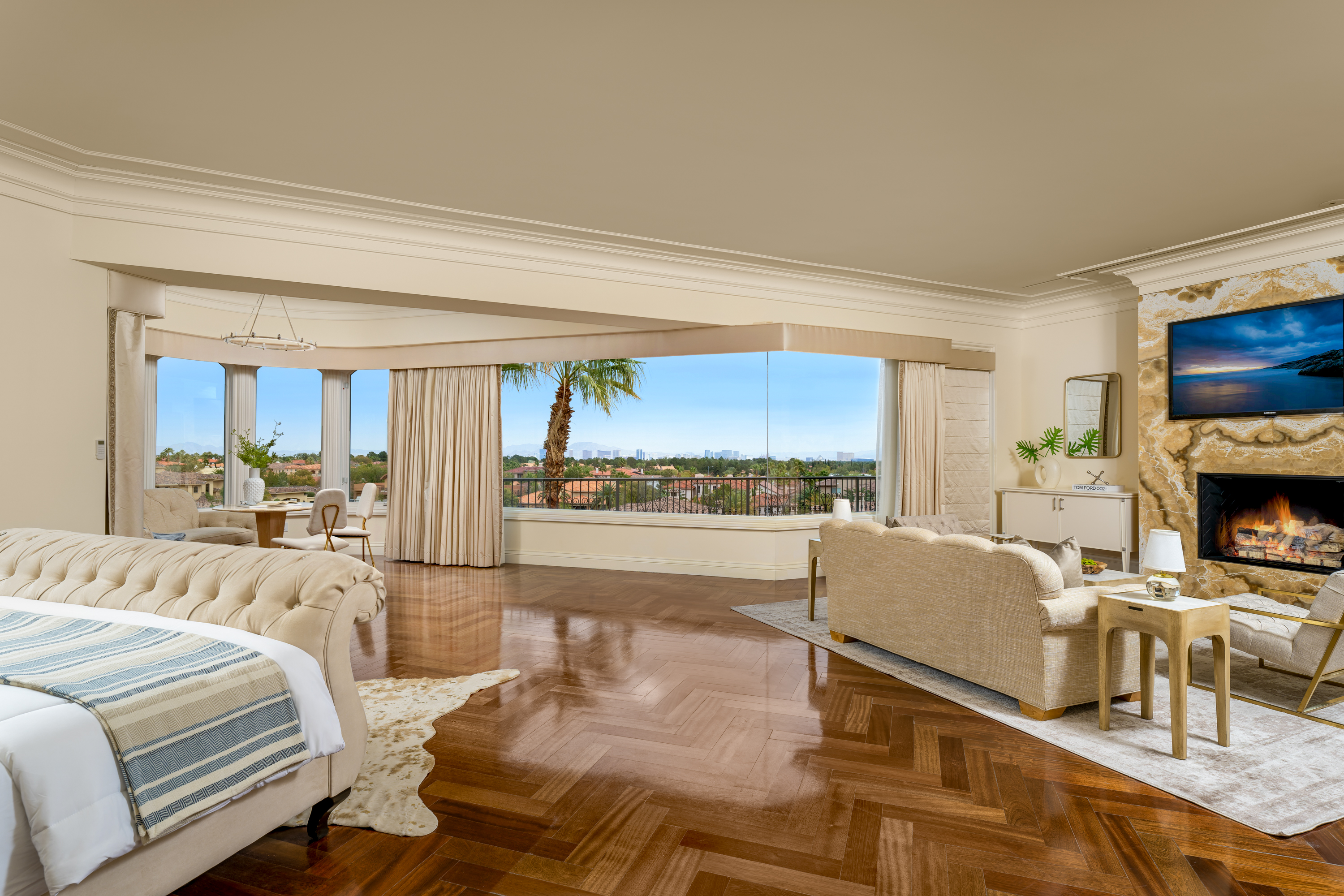 Master Bedroom at a Stately glam estate home in Las Vegas (5114 SHD) — two-story curtains, paired gold-base ottomans, marble fireplace, panoramic view.