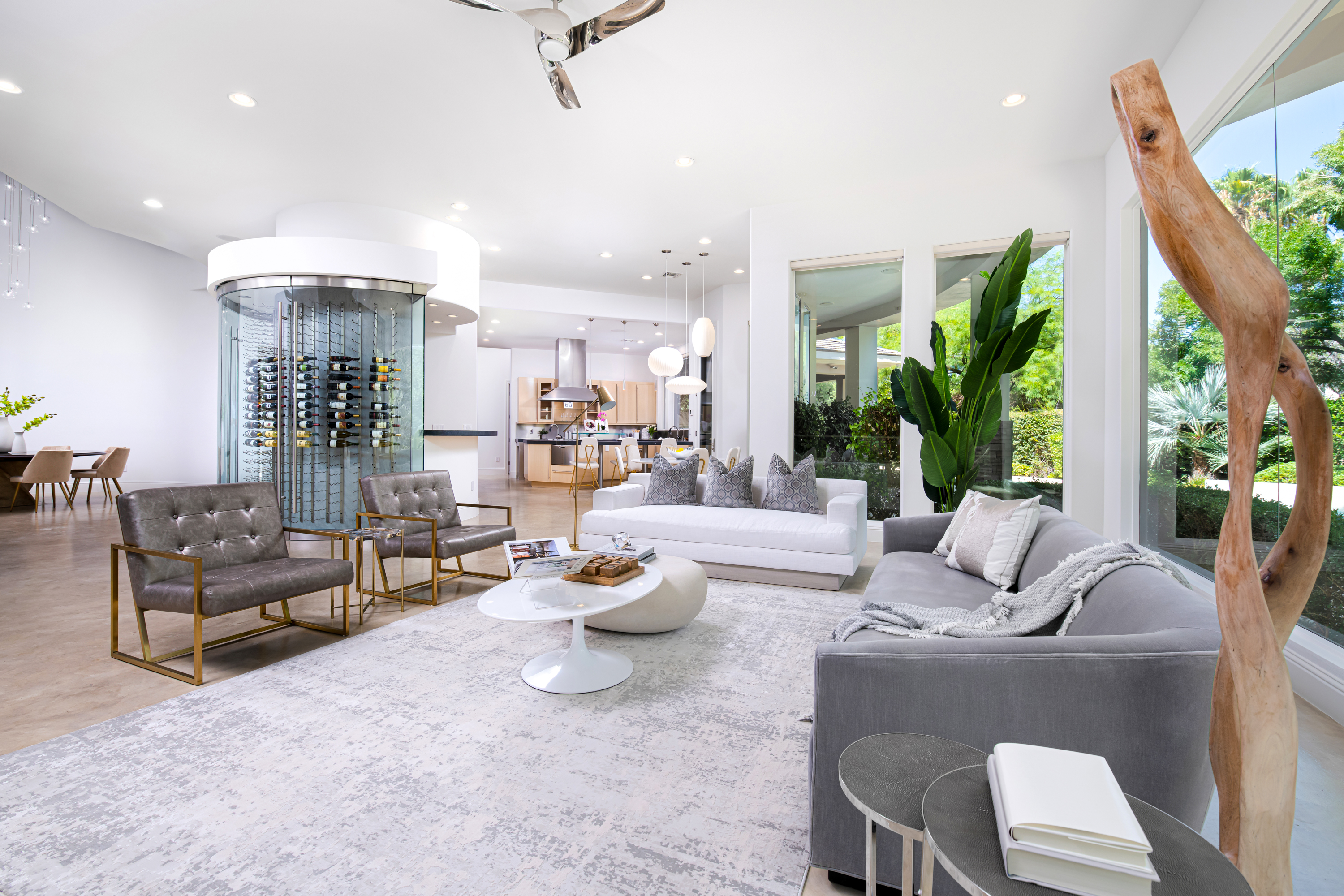 Living Room at a Stately modern luxury w/ wine display home in Las Vegas (9424 TCD) — cylindrical glass wine display, mid-century leather-and-brass chairs, sculptural woo