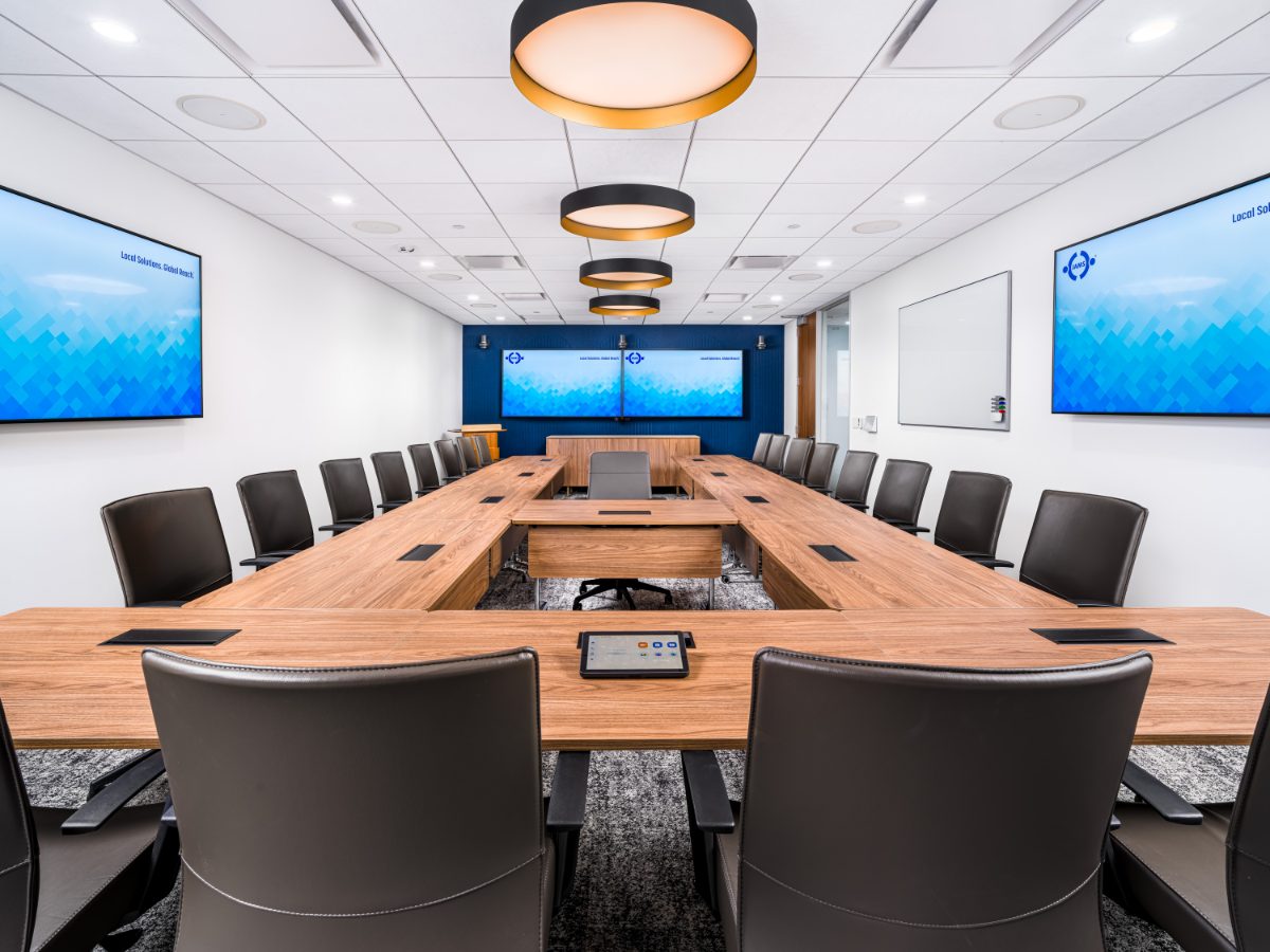 JAMS Dallas boardroom at Sherry Lane Place — U-shaped walnut table, dark leather chairs, three drum pendants, navy reeded back wall, four JAMS displays.