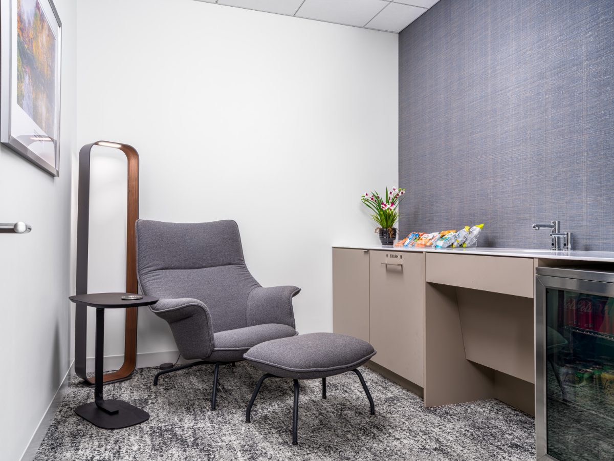 JAMS Dallas quiet room at Sherry Lane Place — grey lounge chair, ottoman, sculptural floor lamp, kitchenette with snacks, mini beverage cooler, grasscloth wall.