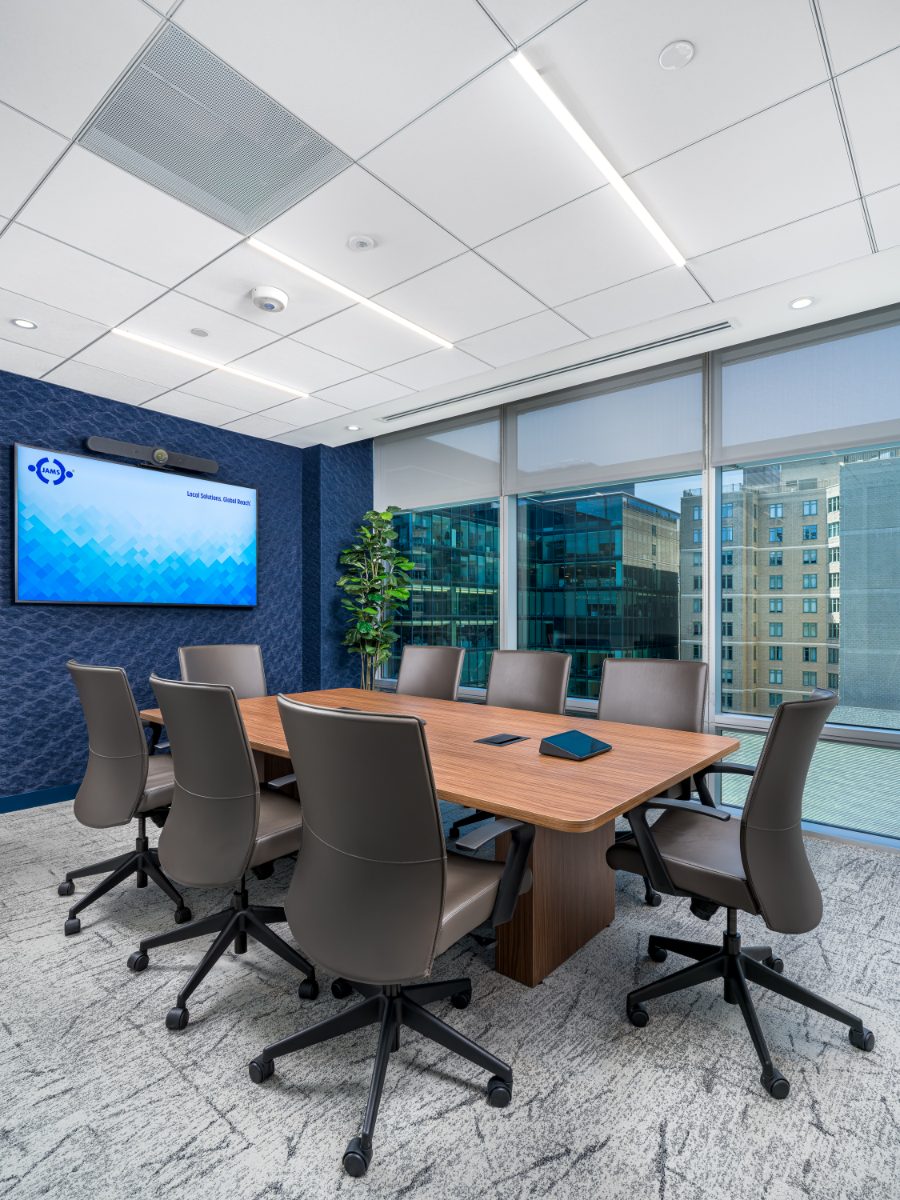 Eight-seat conference room at JAMS Washington, D.C. — walnut table, grey leather chairs, blue accent wall, wall-mounted TV, and floor-to-ceiling K Street windows.
