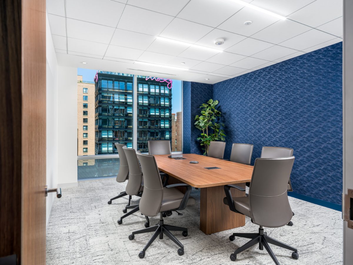 JAMS Washington, D.C. caucus room from the doorway — walnut table, eight grey leather chairs, navy wave-pattern wall, fiddle-leaf fig, and city-view window.