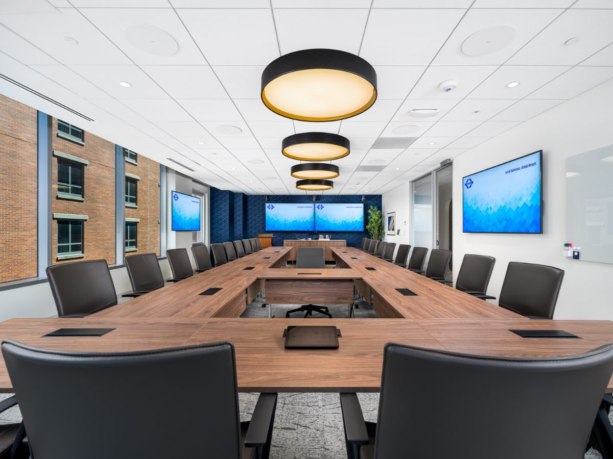 JAMS Washington, D.C. grand boardroom down the length — hollow walnut table, grey leather chairs, drum pendants in perspective, and three JAMS displays at the far end.