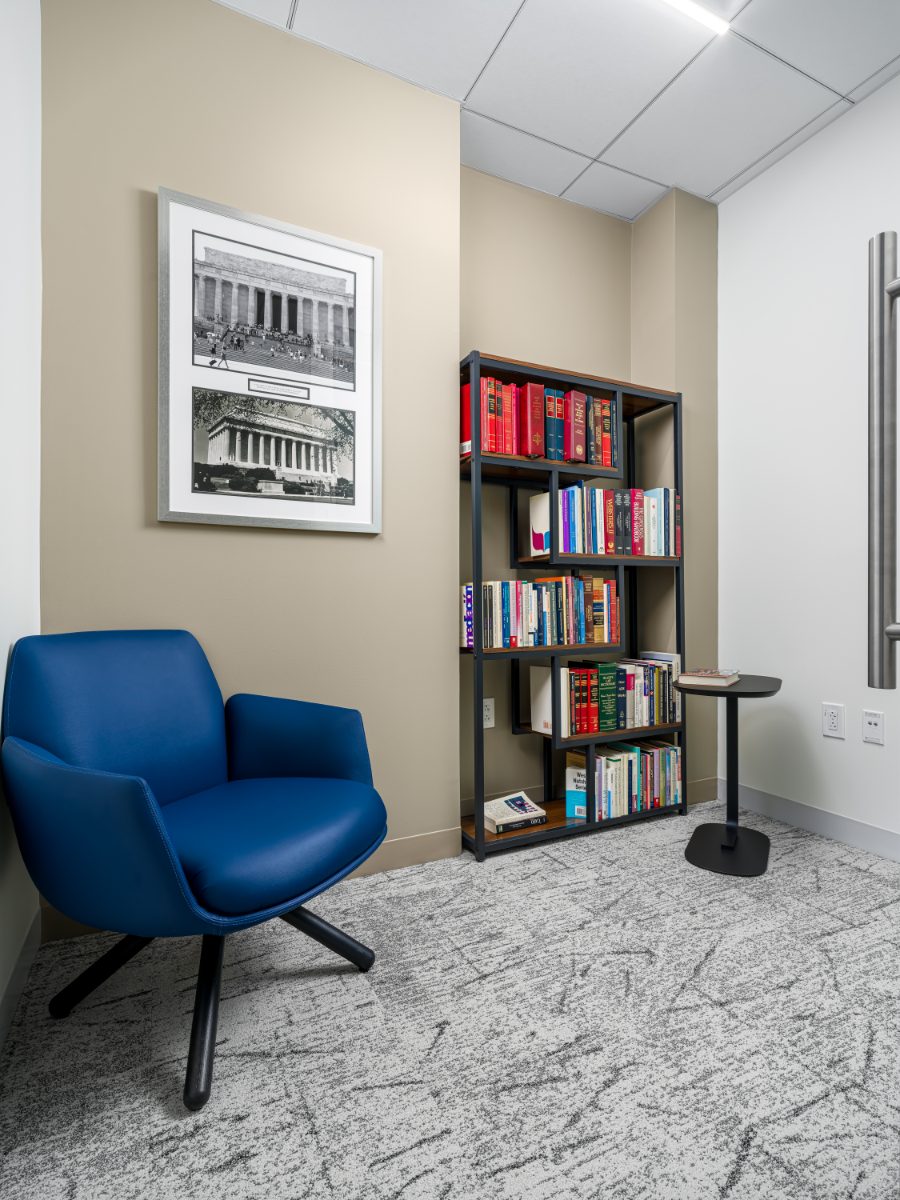 Quiet library nook at JAMS Washington, D.C. — cobalt swivel chair, bookshelf of law and mediation references, framed Lincoln Memorial prints on a beige wall.