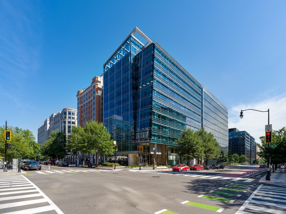 1050 K Street NW — modern glass-and-steel office tower housing JAMS Washington, D.C. Resolution Center, with a crystalline corner prow against a clear blue sky.