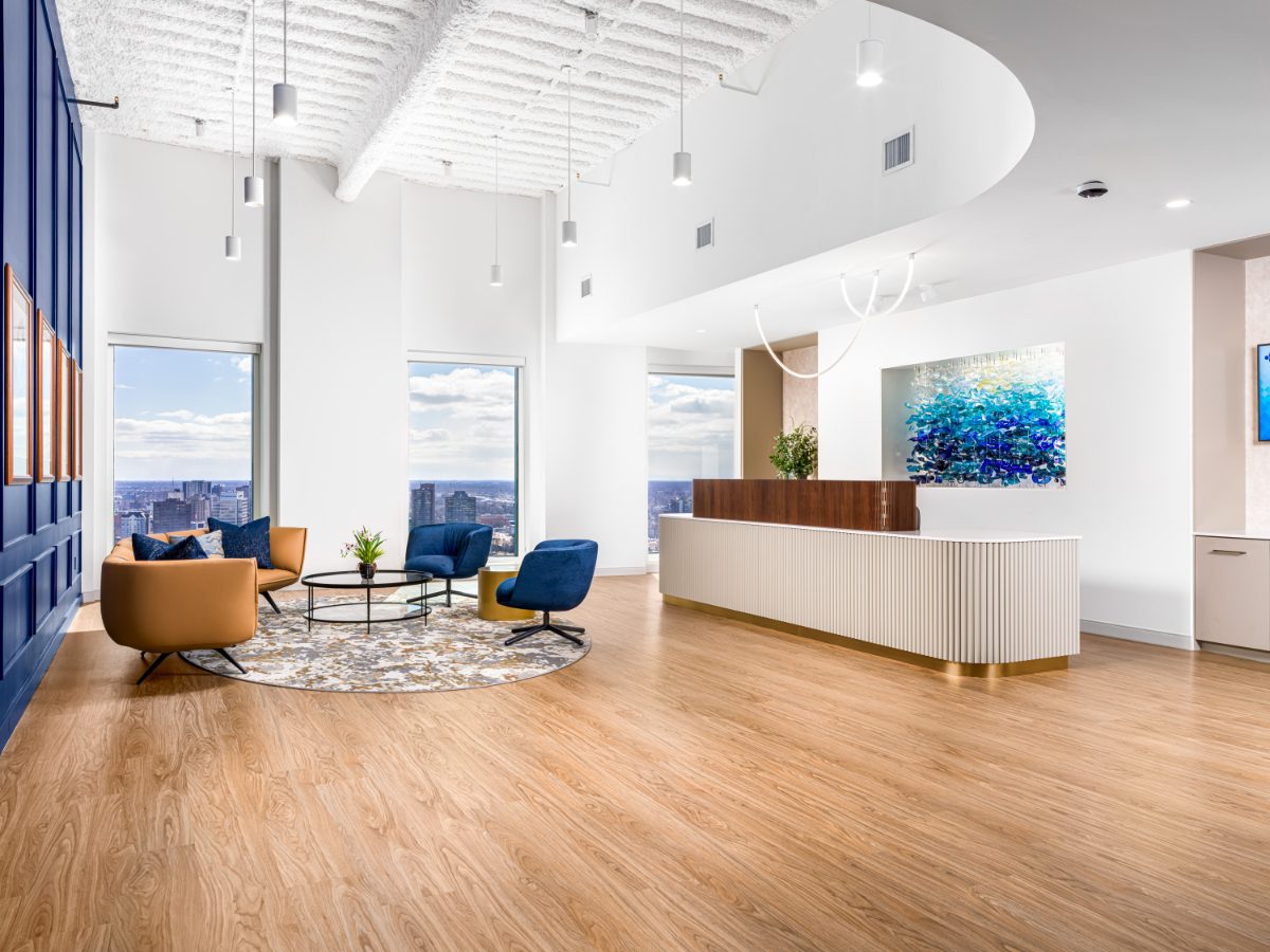 JAMS Detroit reception, wider view — fluted desk in front of a recessed niche holding a cascading blue art-glass sculpture, with cobalt wall and skyline windows.