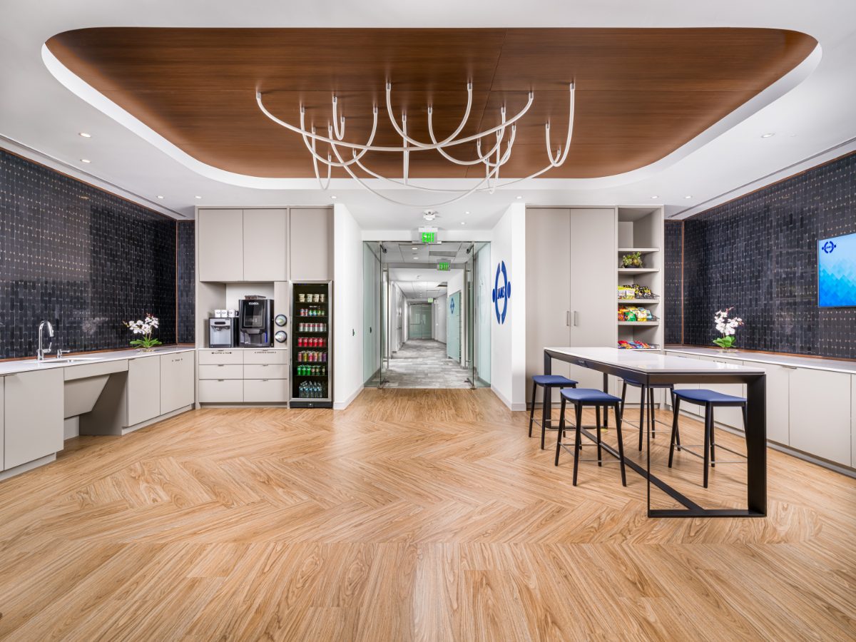 JAMS Cafe at JAMS Detroit — oval walnut ceiling soffit, sculptural white chandelier, blue mosaic backsplash, coffee bar, beverage fridge, and herringbone hardwood floor.