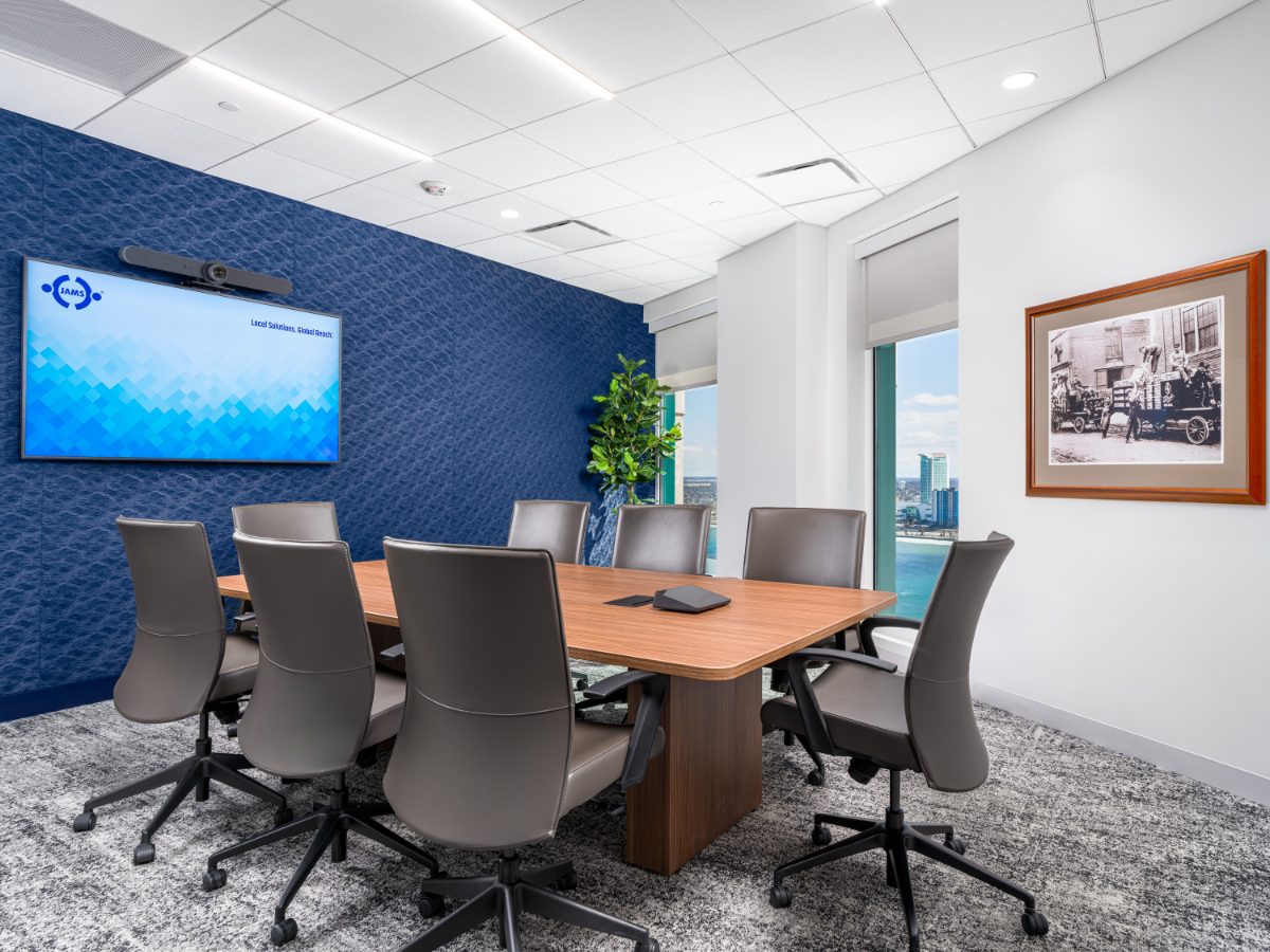 JAMS Detroit conference room — walnut table, grey leather chairs, cobalt textured wall with JAMS display, framed historic Detroit print, and Windsor-across-river view.
