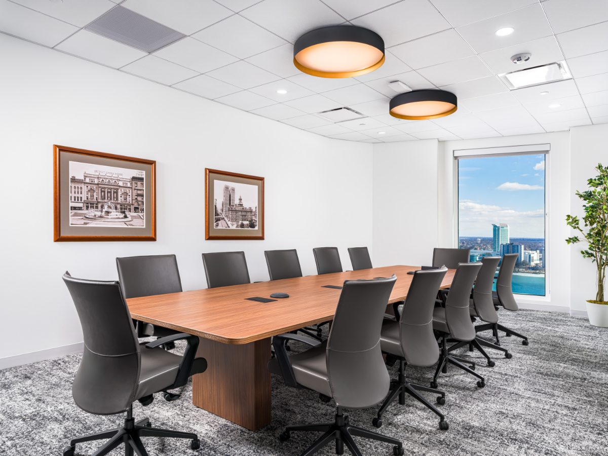 JAMS Detroit conference room — walnut table, twelve grey leather chairs, drum pendants, framed Detroit Opera House sepia prints, and a Caesars Windsor view window.
