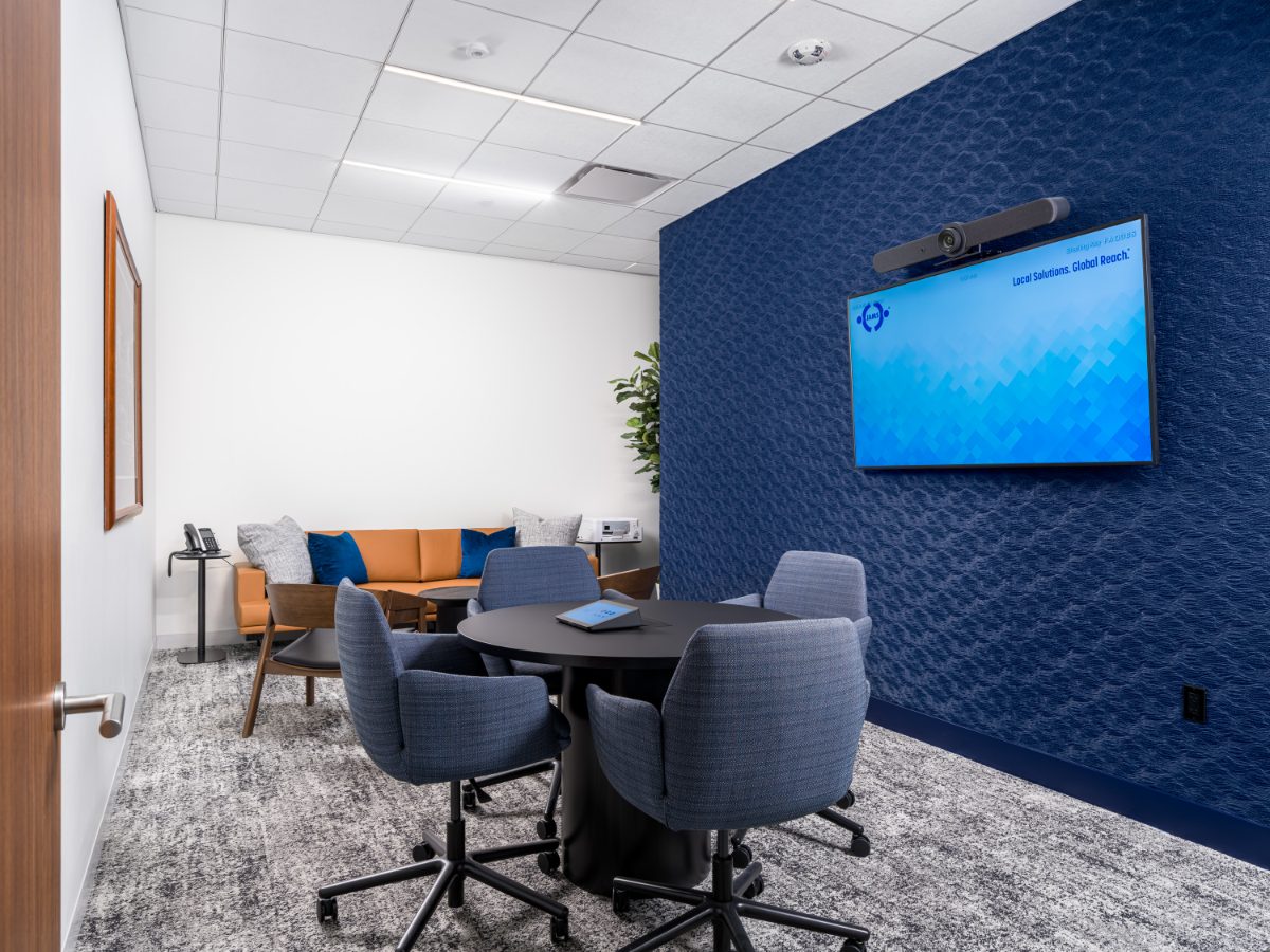 Caucus suite at JAMS Detroit — round black table with four navy upholstered chairs, cobalt fabric wall with JAMS display, and a cognac leather sofa lounge in the corner.
