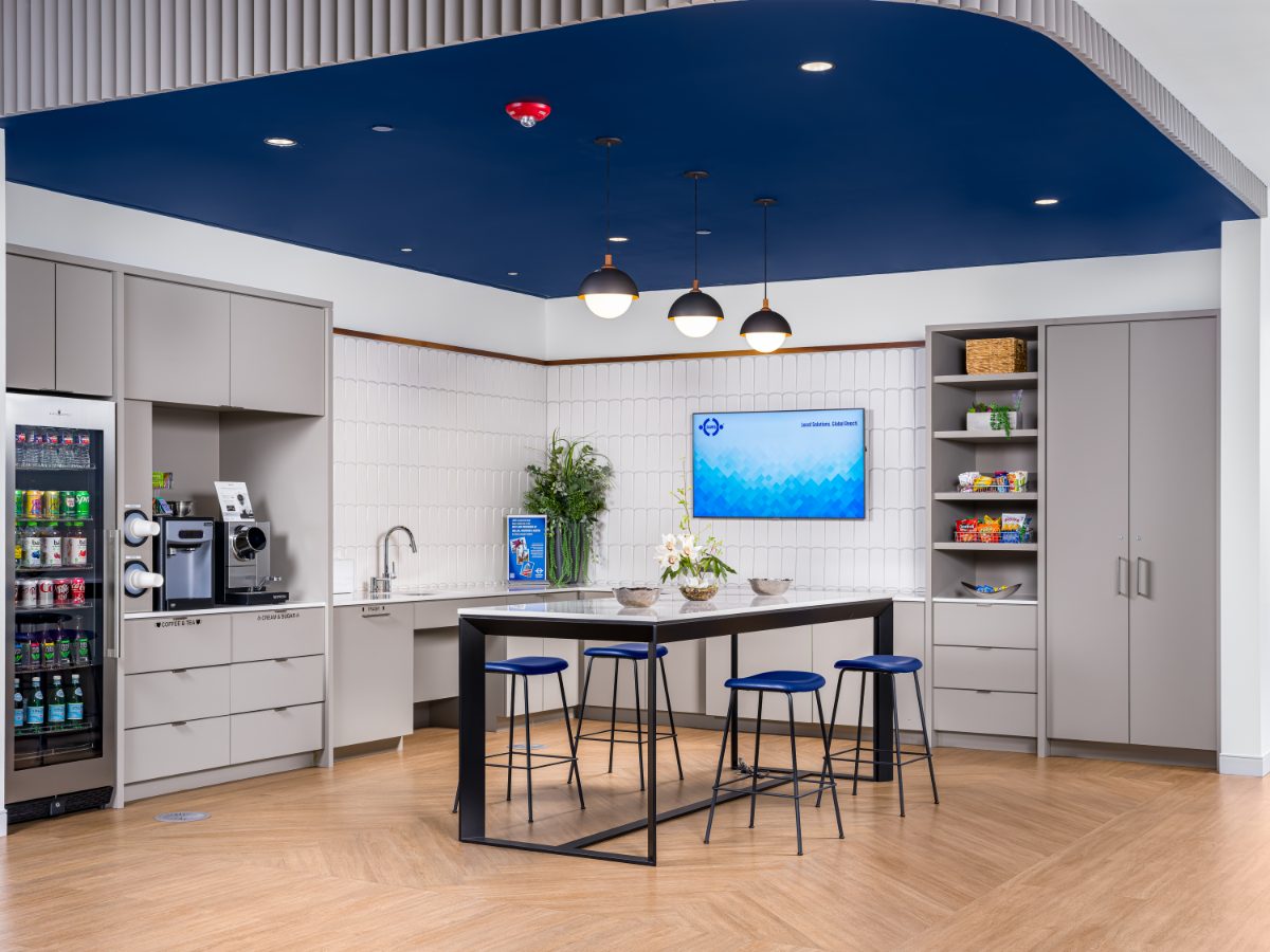 JAMS Cafe at JAMS Houston — black island with four navy stools, three globe pendants under a navy ceiling, arched-tile backsplash, beverage fridge, and snack pantry.