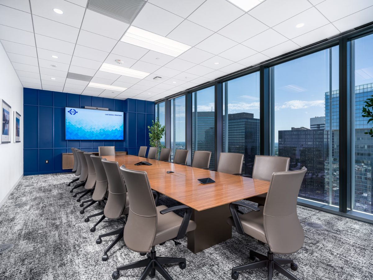 Skyline conference room at JAMS Houston — walnut table, grey leather chairs, cobalt panel wall with JAMS display, and floor-to-ceiling skyline windows.