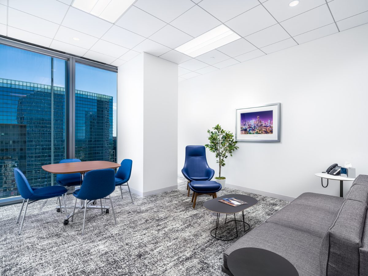 Mediation room at JAMS Houston — oval walnut table with four blue chairs, blue lounge chair with ottoman, grey sofa, and framed Houston night skyline print.