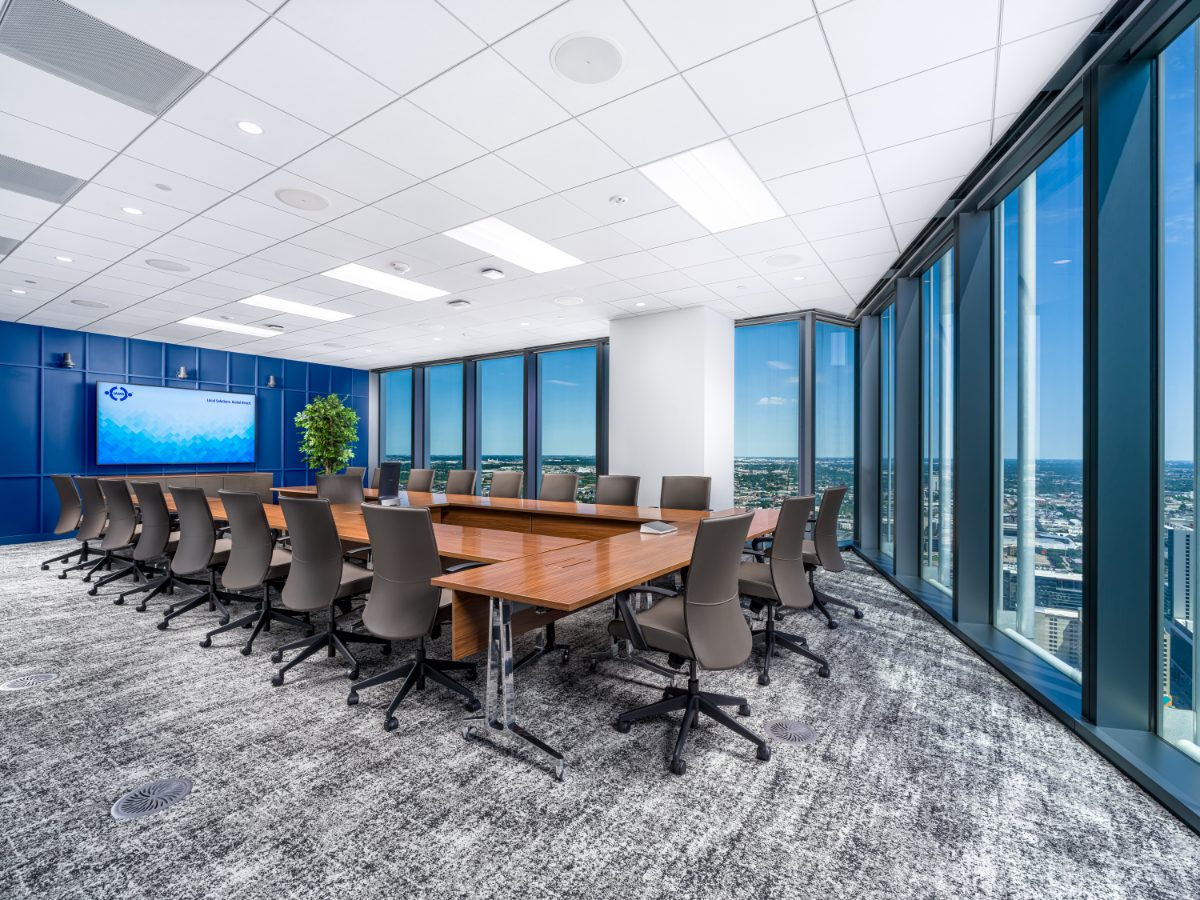 Grand boardroom at JAMS Houston — walnut U-shape table, twenty grey leather chairs, cobalt panel wall with JAMS display, and corner skyline windows.