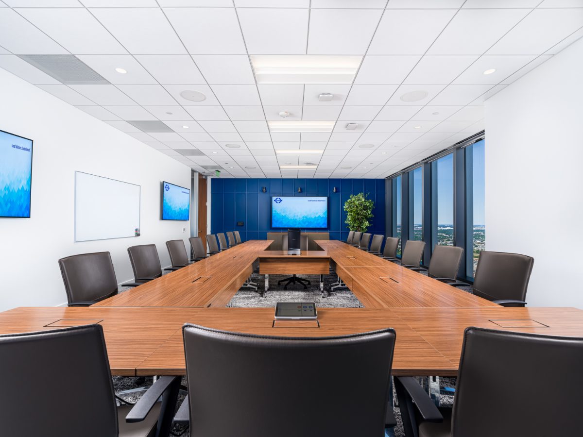 JAMS Houston grand boardroom from the open end — U-shape walnut table, leather chairs, three JAMS displays, and Houston horizon windows on the right.