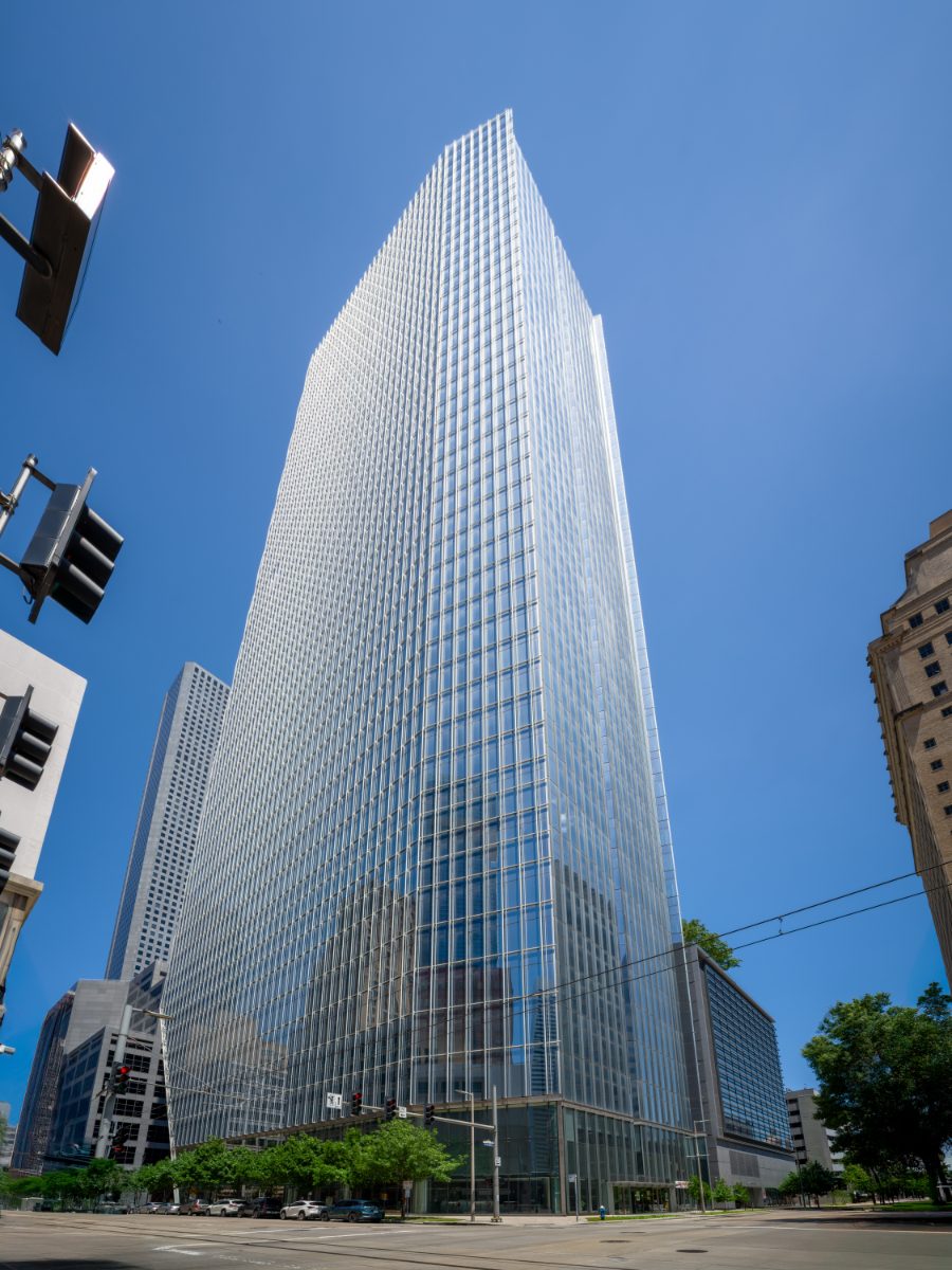 609 Main from street level — Pickard Chilton glass tower rising forty-eight floors into a clear Houston sky, with a smaller historic neighbor at the right edge.