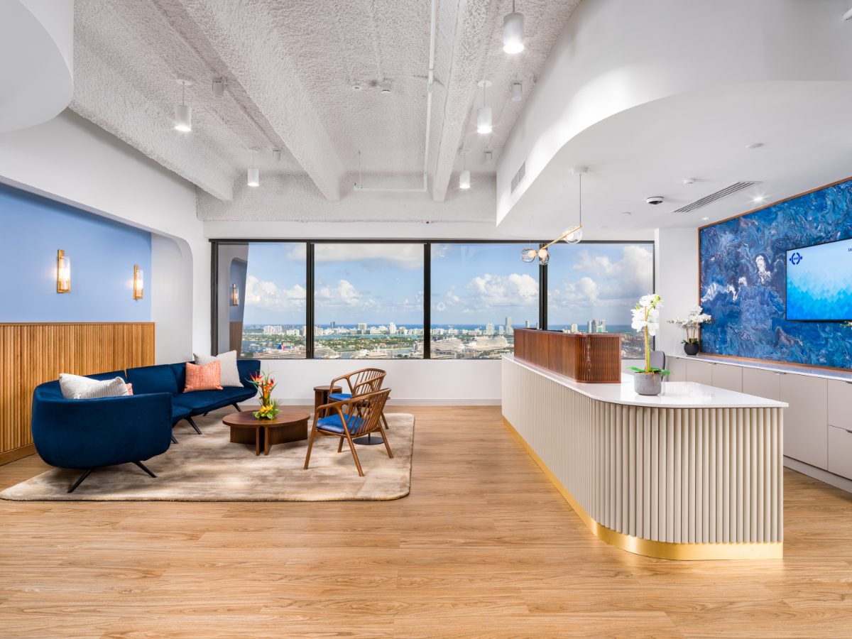 Reception lounge of the JAMS Miami Resolution Center on the 36th floor of One Biscayne Tower — a curved white-quartz reception desk with fluted cream base and brass kick plate bene