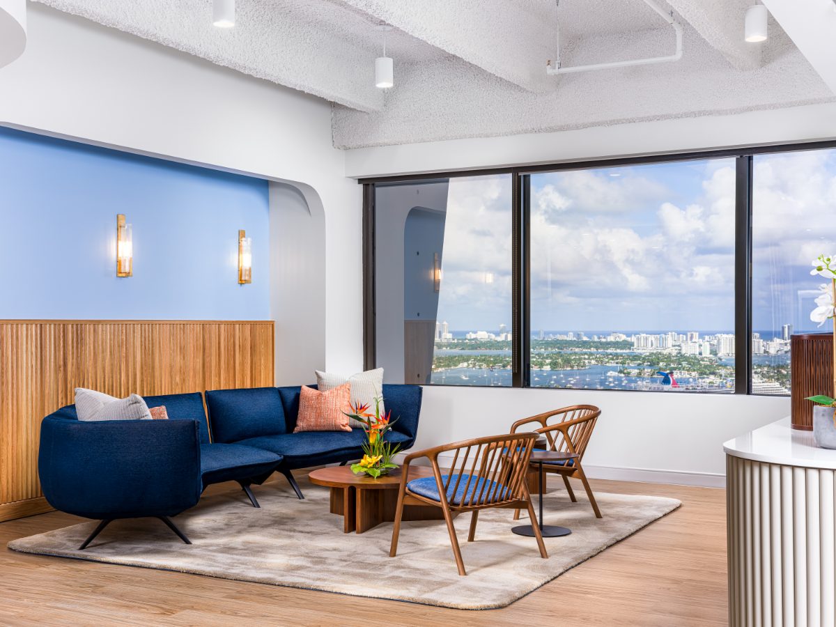 JAMS Miami reception lounge on the 36th floor of One Biscayne Tower — navy velvet sectional, wood spindle chairs, walnut coffee table, window onto Biscayne Bay.