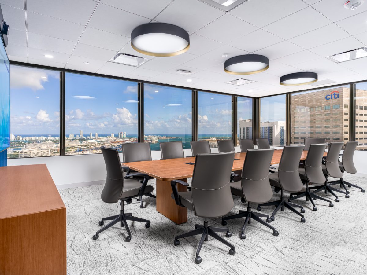 JAMS Miami conference room on the 36th floor of One Biscayne Tower — walnut table, grey leather chairs, brass pendants, windows over the Port of Miami.