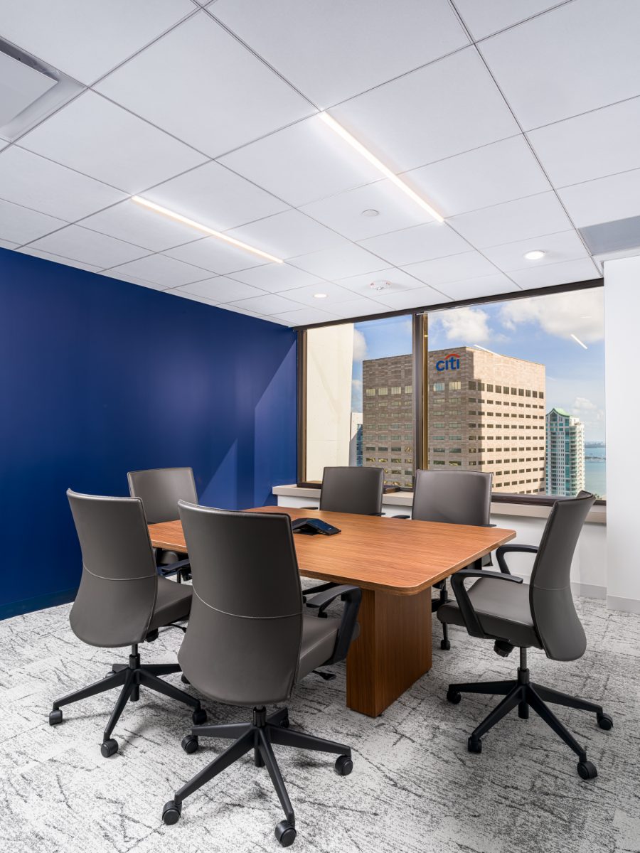 JAMS Miami caucus room on the 36th floor — six grey leather chairs around a walnut table, cobalt accent wall, window onto the Brickell skyline and Citi tower.