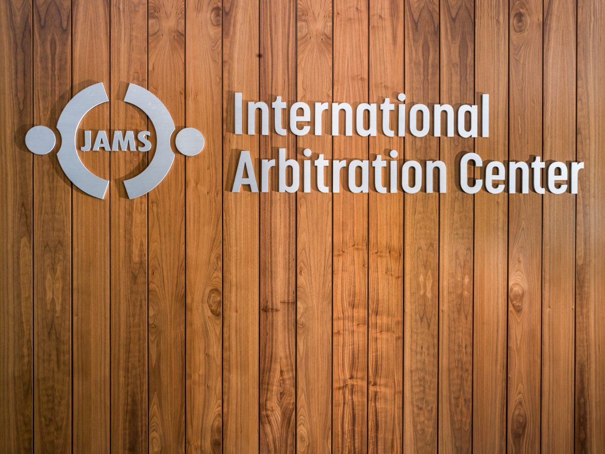 JAMS International Arbitration Center brushed-aluminum signage on walnut paneling at the Miami Resolution Center — dimensional logo mark and letterforms.