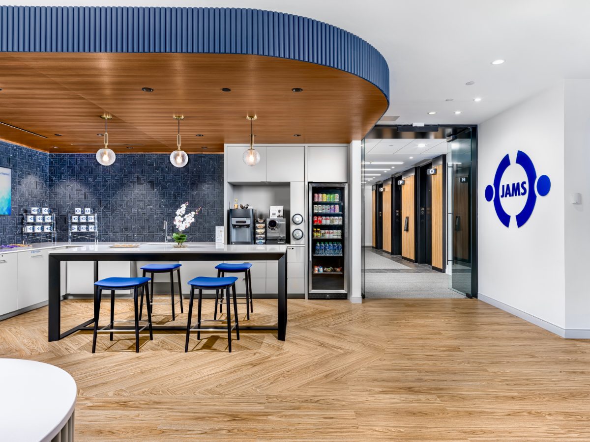 JAMS MN main entry — JAMS Café with navy mosaic backsplash, walnut soffit, glass globe pendants, blue bar stools, opens onto the elevator lobby with JAMS logo.