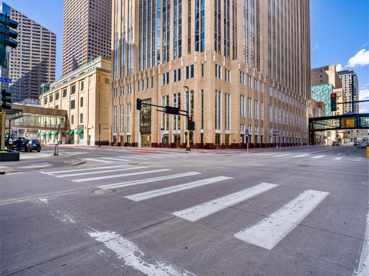 Wells Fargo Center entrance at 90 S. Seventh, Minneapolis — Art Deco limestone facade, three sets of brass-framed double doors, American flag in the central window.