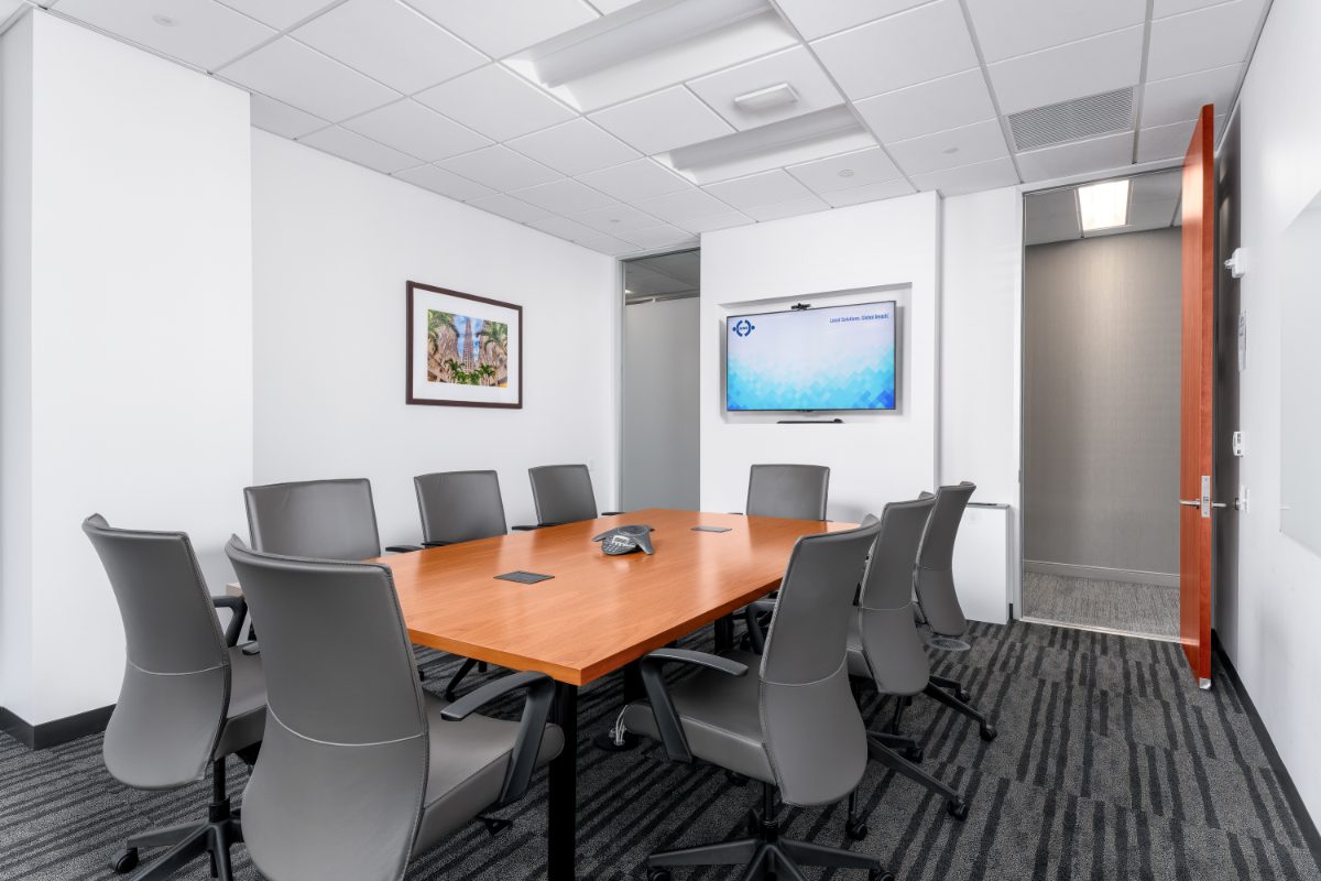 JAMS IAC Conf Room 12 — 10-seat cherry table on black trestle base, grey leather chairs, framed Chrysler Building print on left wall, JAMS display on back.