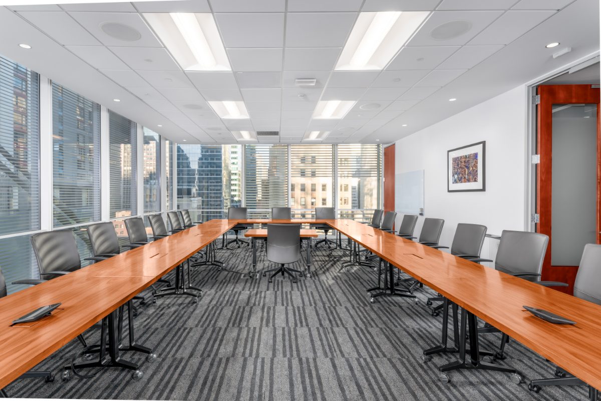 Boardroom 7 at JAMS NY 16th Floor — reverse view across the cherry horseshoe to a louvered window wall of sunlit Midtown towers, framed mosaic, red door.